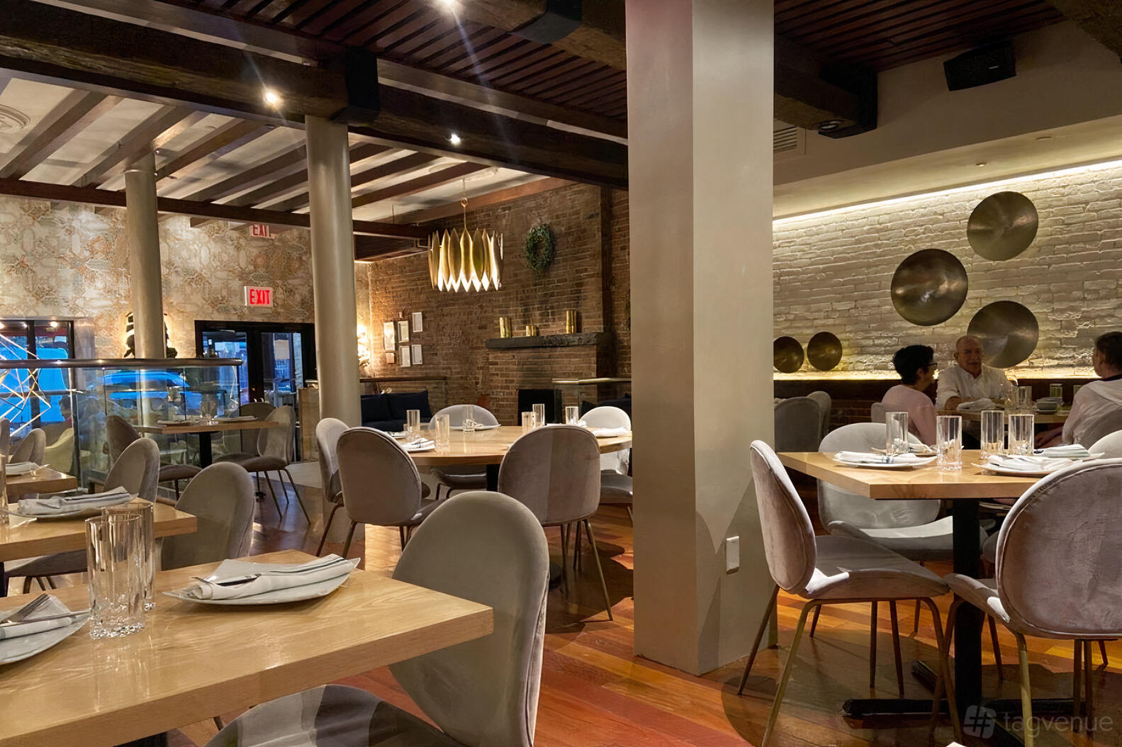 An event space with exposed brick walls, round wooden tables, and metallic wall accents at Yara.