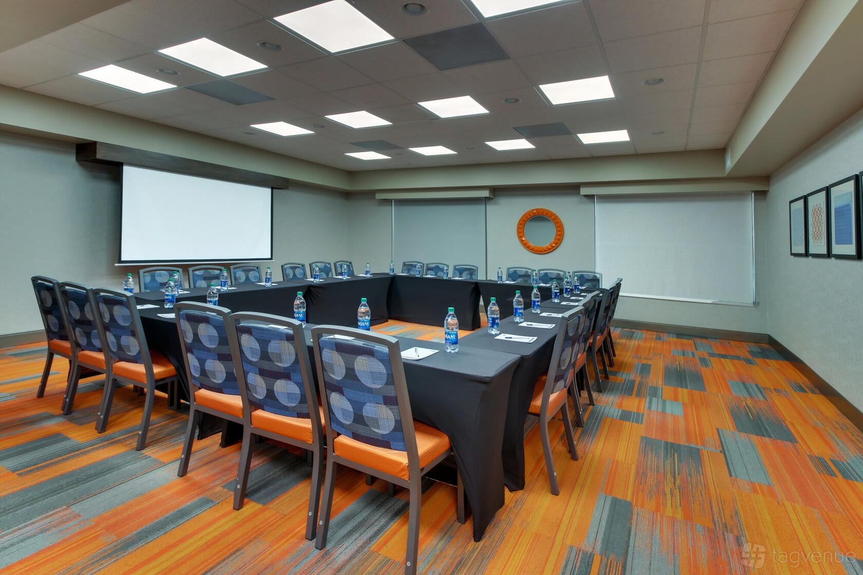 A meeting room with U-shaped tables, patterned chairs, water bottles, and a ceiling projector at Holiday Inn Express Atlanta N-Perimeter Mall.