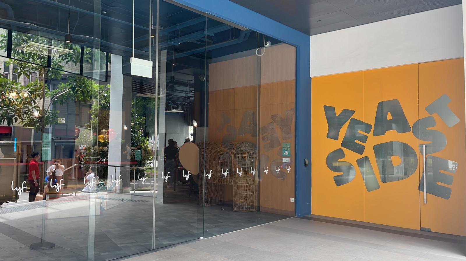 A restaurant entrance with floor-to-ceiling glass doors, indoor plants, and bright mural walls at Yeast Side LYF at Farrer.