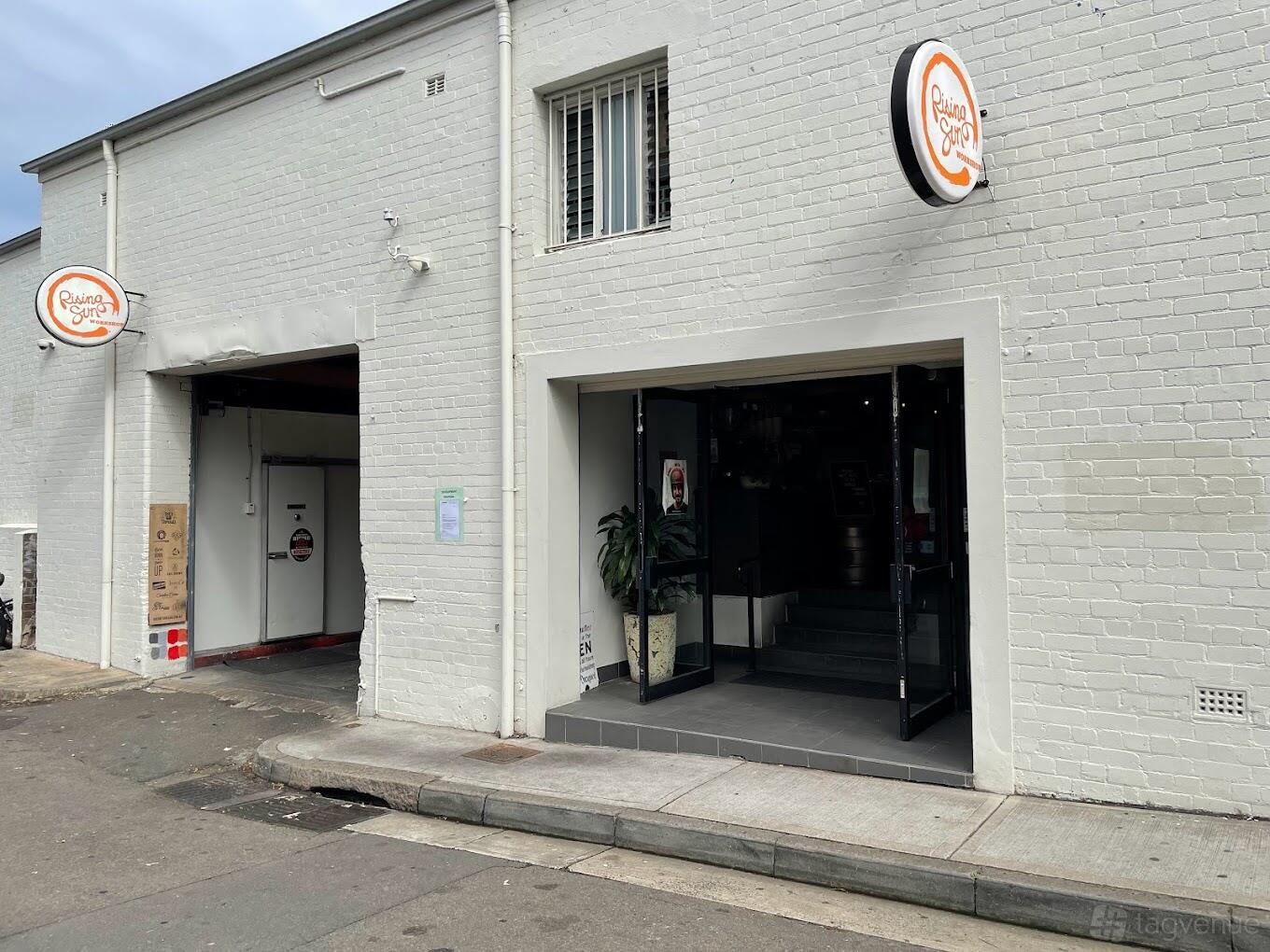 A restaurant with white brick exterior walls, wide entry doors, and a round Rising Sun Workshop sign above the entrance.