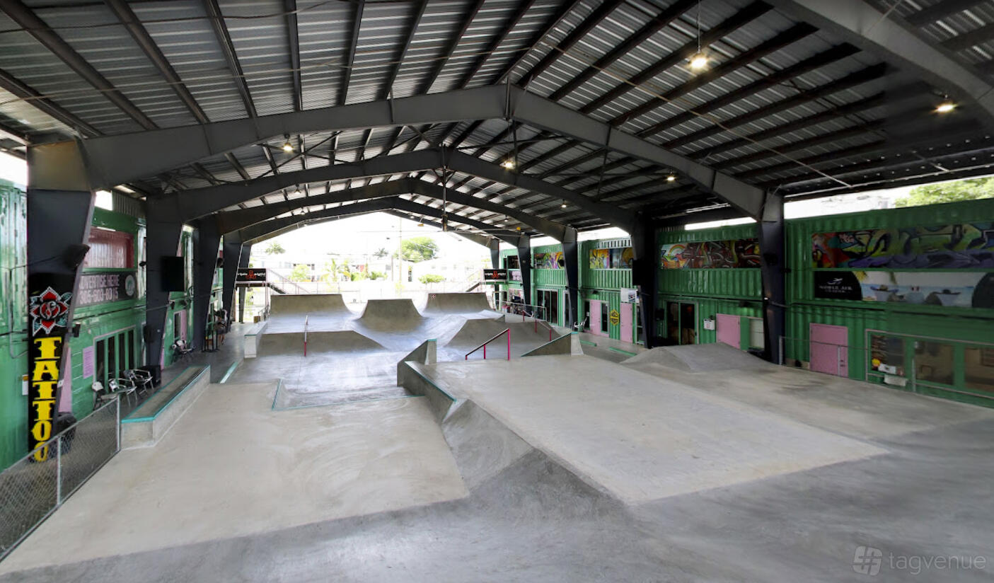 An indoor skate park with concrete ramps, rails, and graffiti-covered shipping containers at Skatebird Miami.