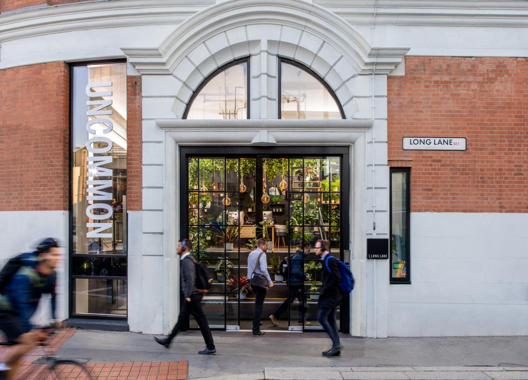 A coworking space with a glass entrance, arched doorway, and greenery visible inside at Uncommon Borough.