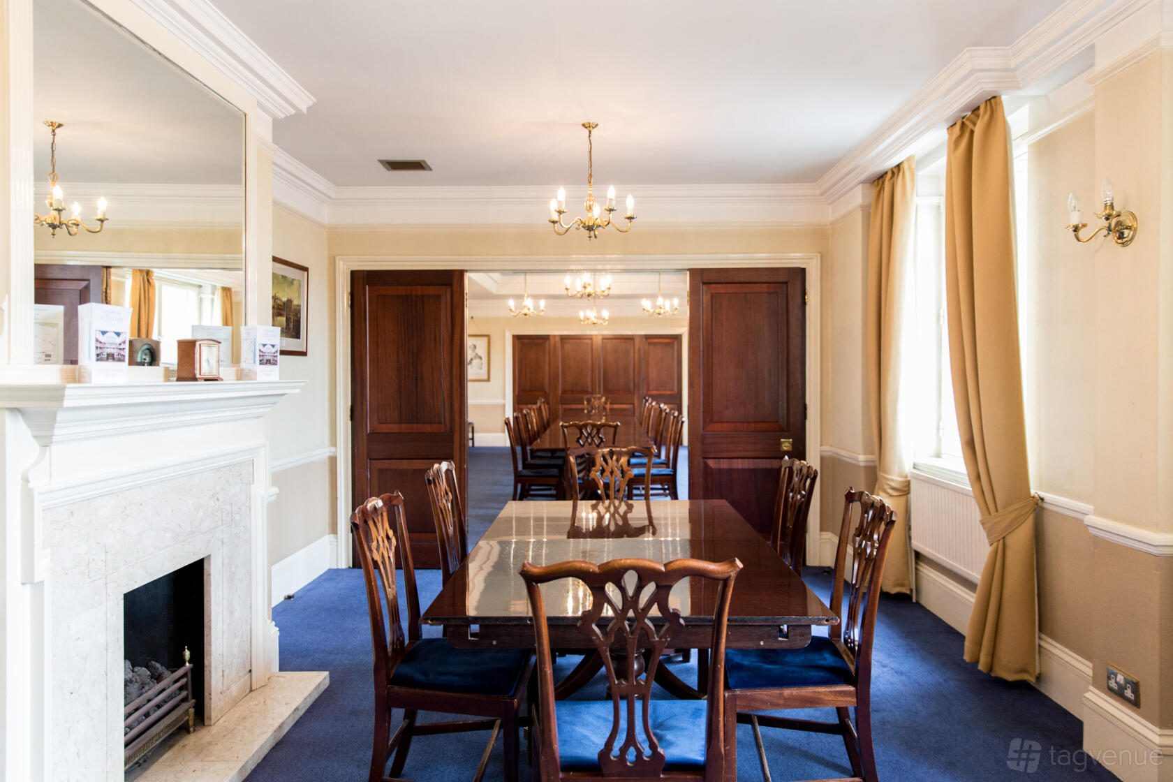 An event venue with a rectangular wooden table, classic chairs, chandeliers, and a fireplace at London Scottish House.
