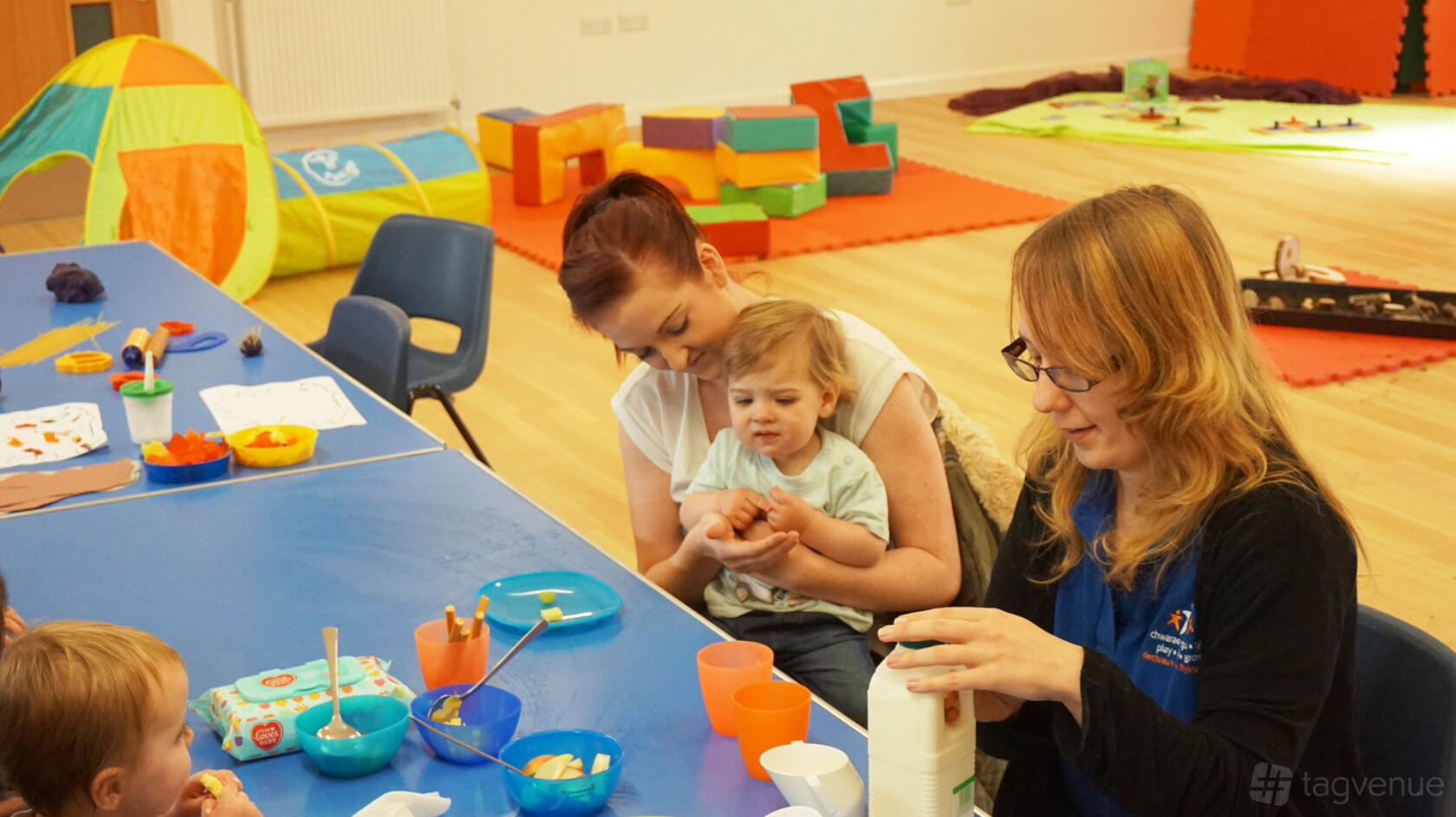 An event space in a community centre with a play area, wooden floors, and tables set for snacks at Castleland Community Centre.