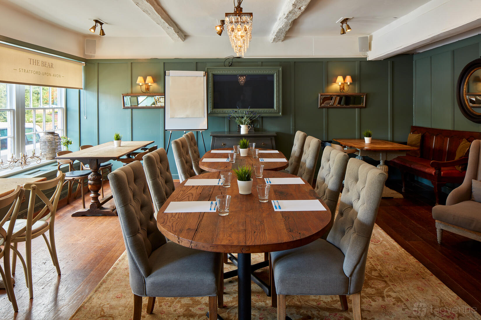 A dining room with wooden tables, upholstered chairs, and chandeliers at Bistrot Pierre Stratford-upon-Avon.