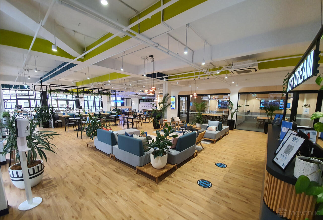 An open event space with lounge seating, potted plants, wood flooring, and large windows at JustCo at Flinders St.