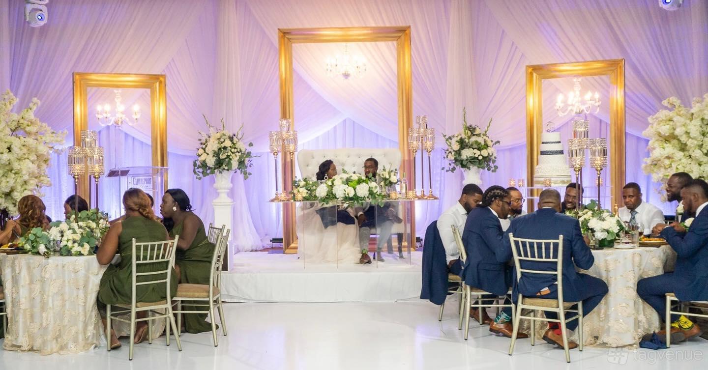A banqueting hall with draped white walls, gold accents, chandeliers, and banquet tables at Julius Event Centre.
