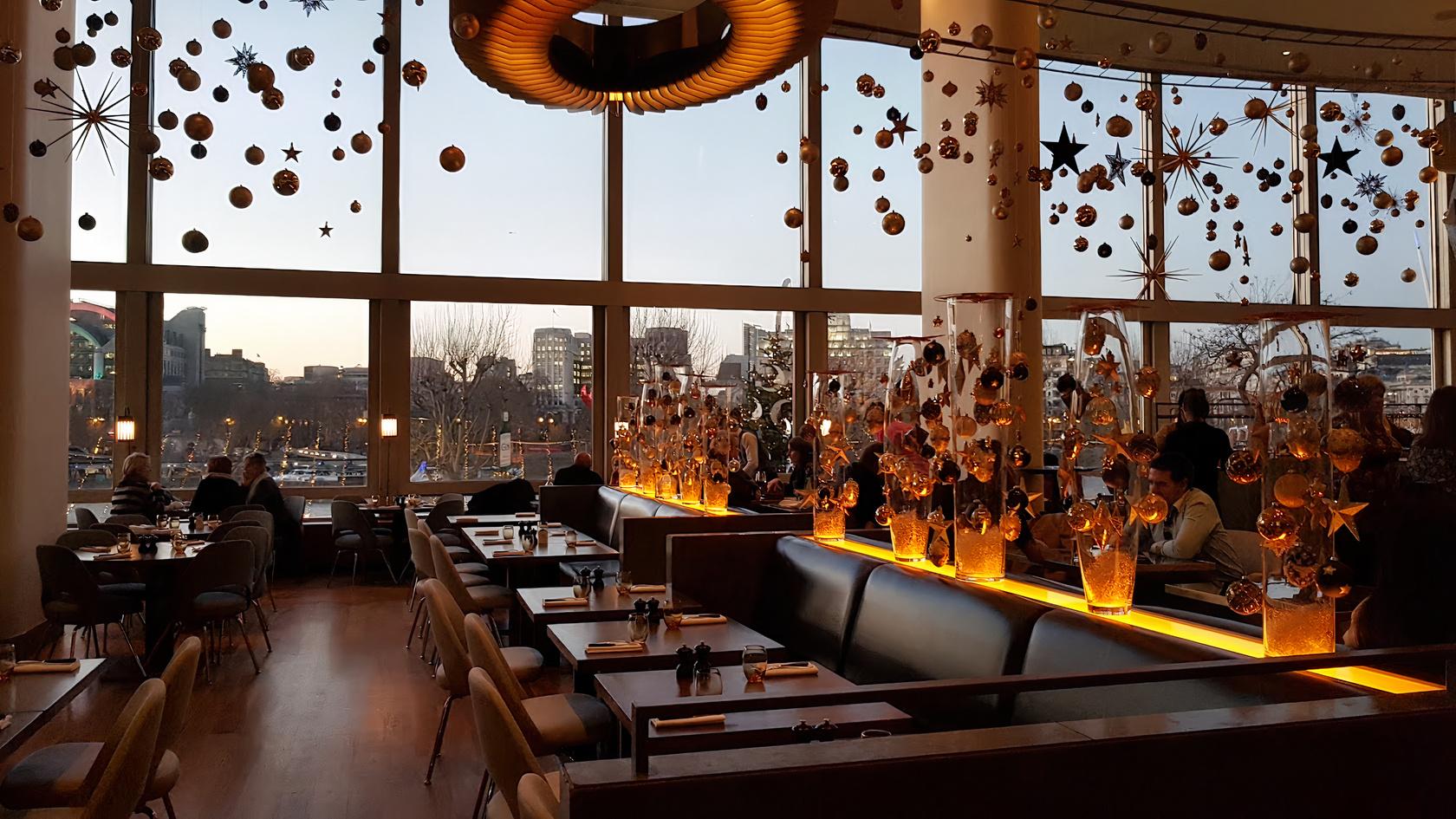 A restaurant with floor-to-ceiling windows, decorative hanging ornaments, and banquette seating at Skylon.