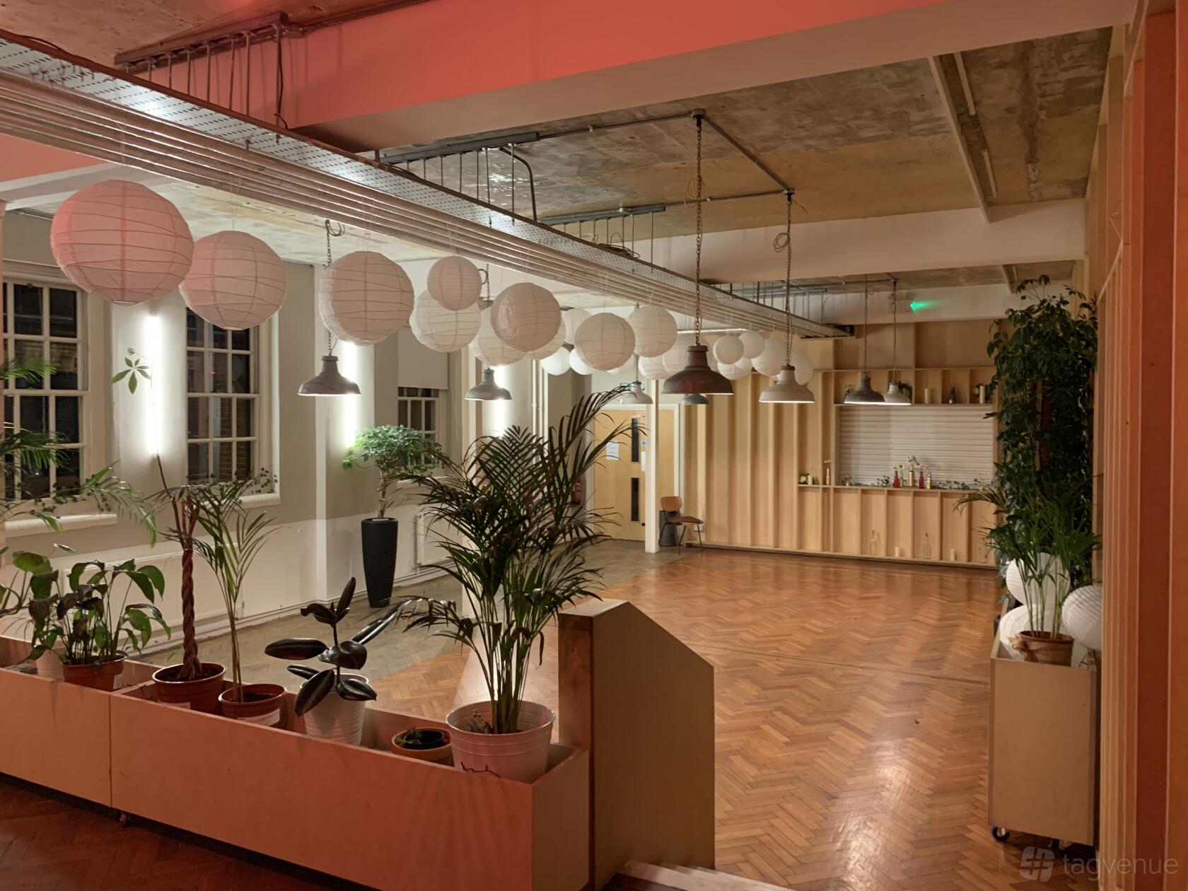 An event venue with wood flooring, potted plants, paper lanterns, and large windows at Core Clapton.