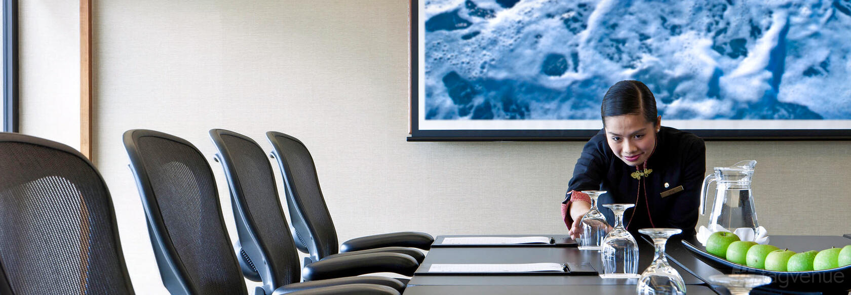 A boardroom with mesh-back chairs, writing pads, and glassware on a conference table at Pan Pacific Singapore.