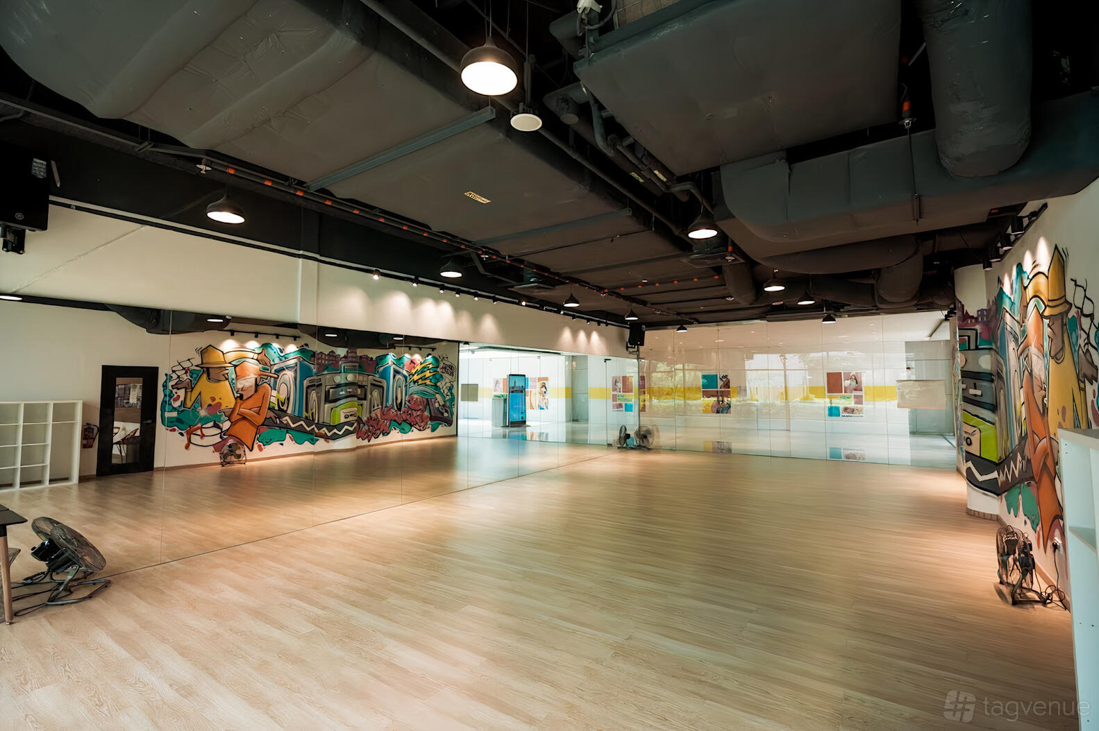 A dance studio with light wood floors, mirrored walls, and colorful graffiti art at Danz People.