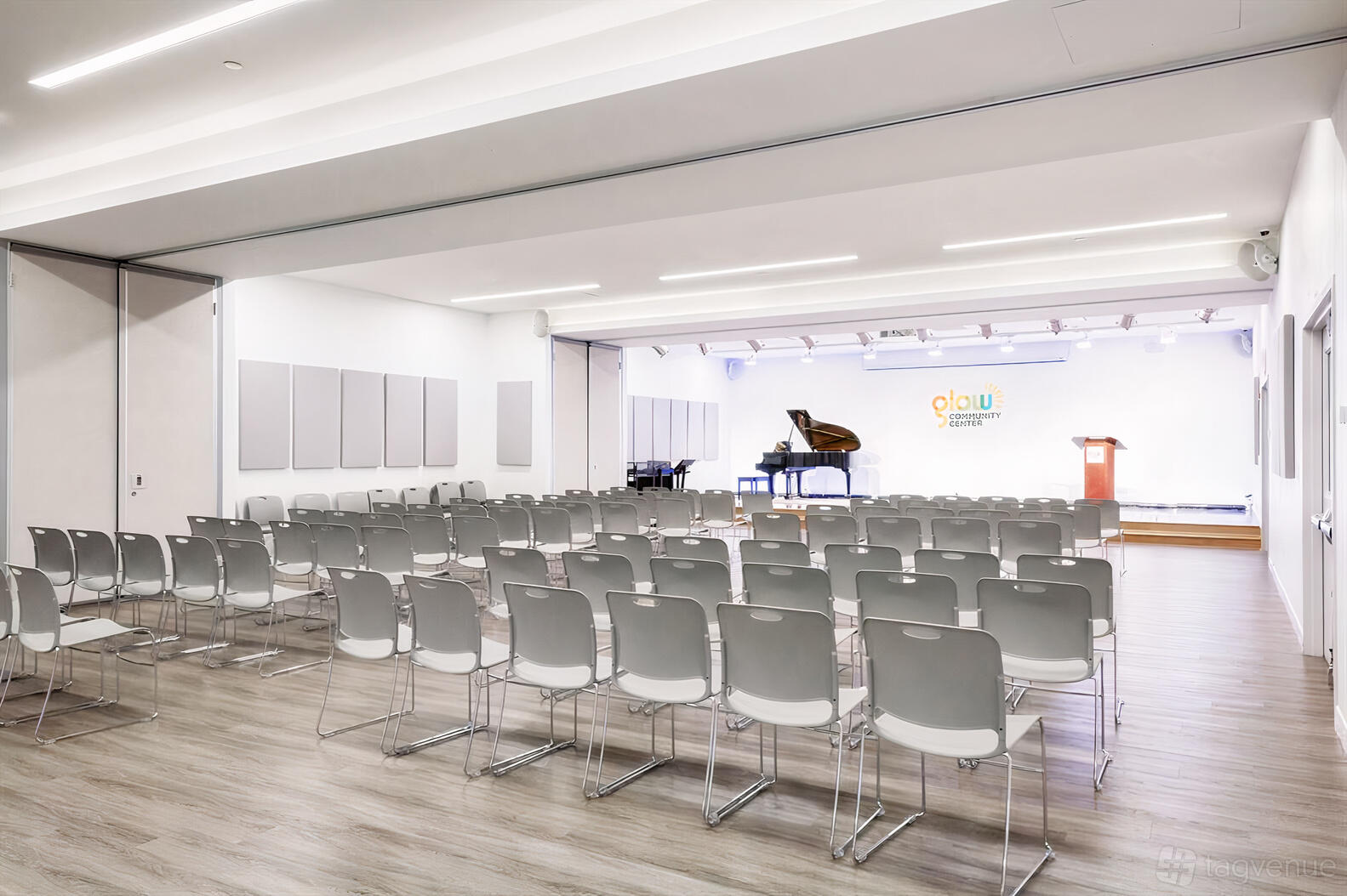 A community centre with rows of gray chairs facing a stage with a grand piano and podium at Glow Cultural Center.