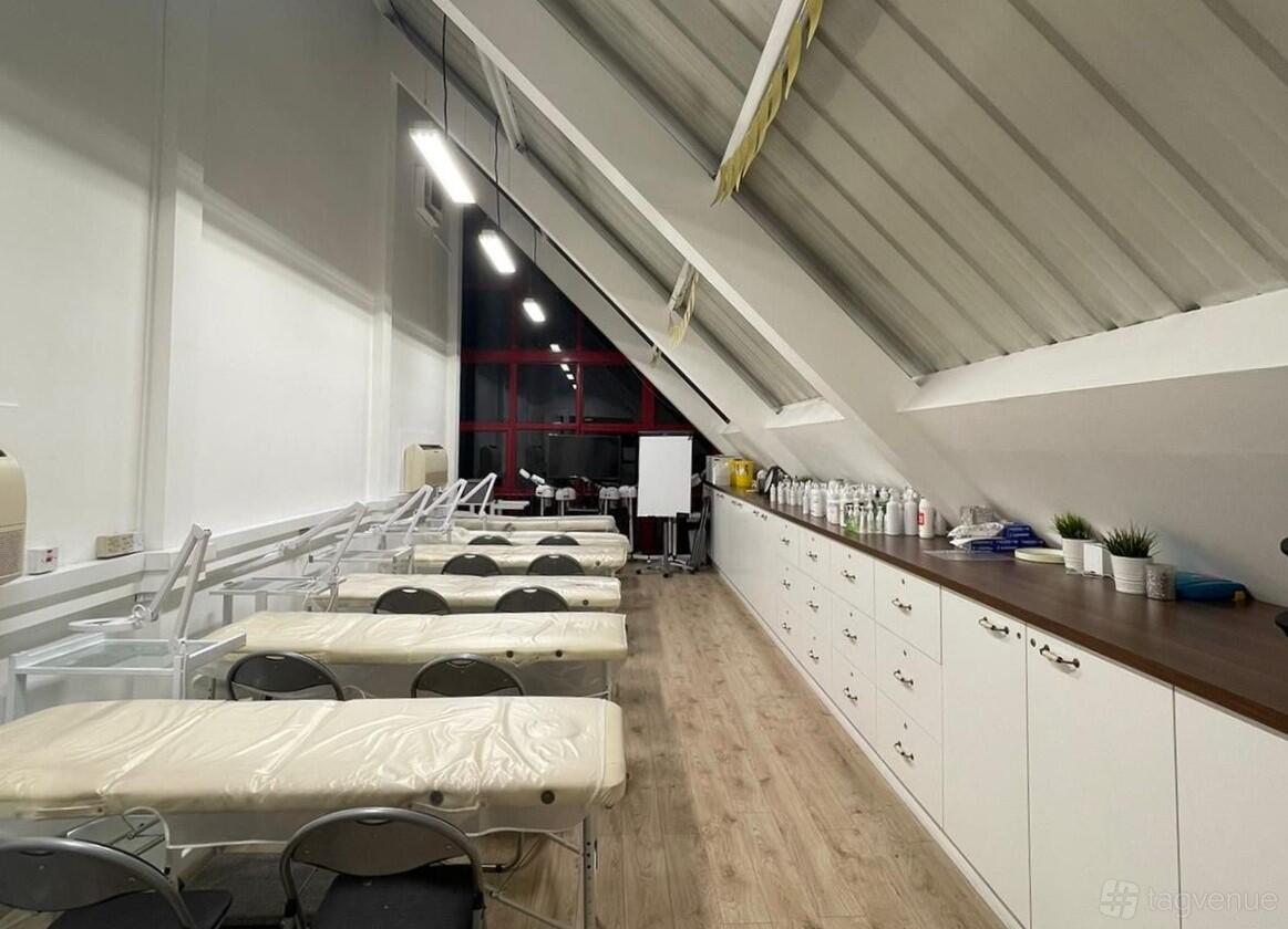 A training room with treatment beds, folding chairs, long countertops, and shelves with beauty products at Moda Donna PMU & Beauty Academy.