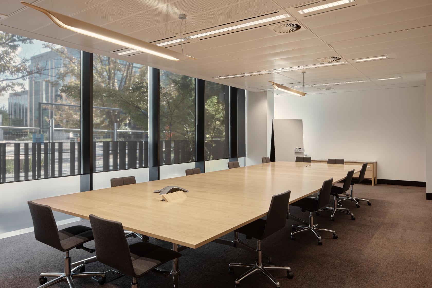 A meeting room with a long wooden conference table, black chairs, floor-to-ceiling windows, and natural lighting at Flex by ISPT at 4 National Circuit.