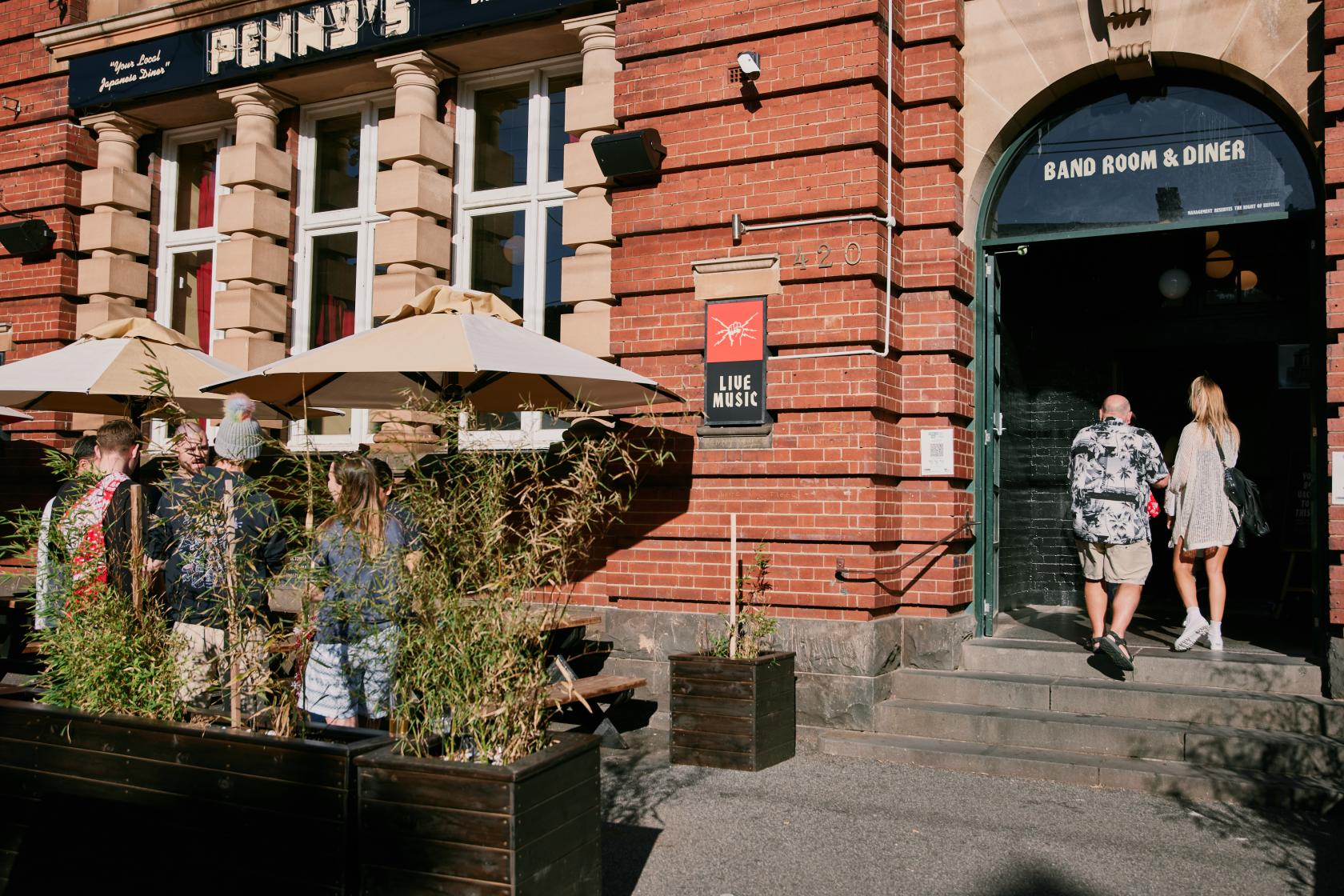 A pub with outdoor wooden tables shaded by large umbrellas and brick facade at The Penny Black