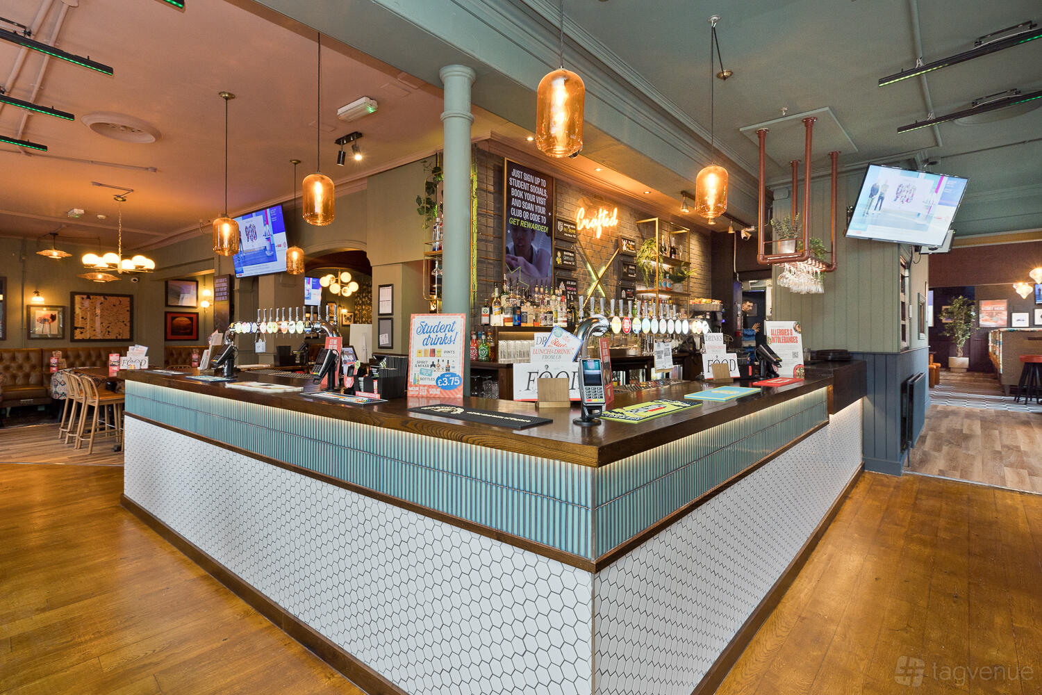 A pub with a large wooden bar, hexagon tile accents, overhead lighting, and beer taps at Bristol Pear, Birmingham.