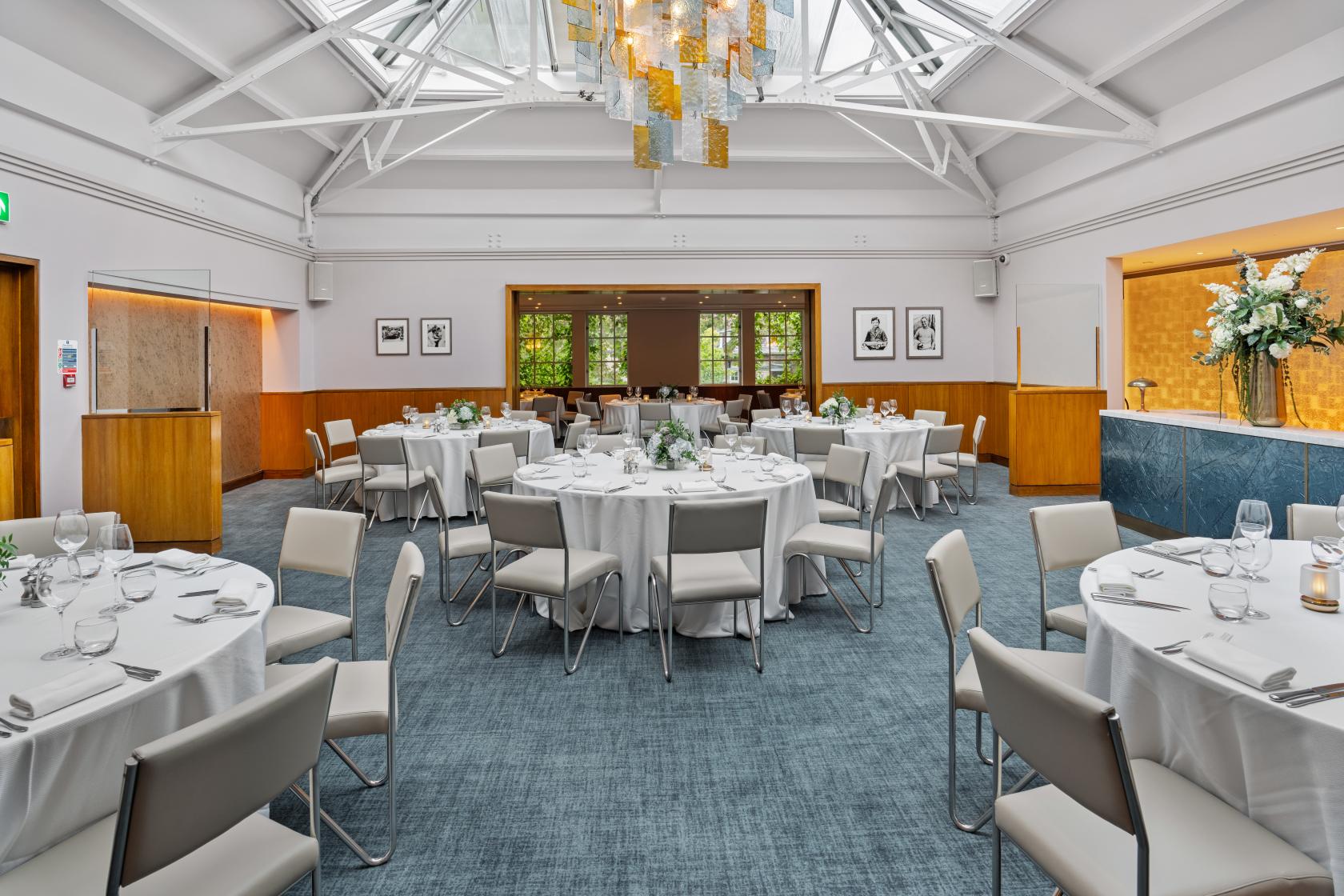 An event space in a restaurant with round tables draped in white linens under a glass skylight at Bluebird.