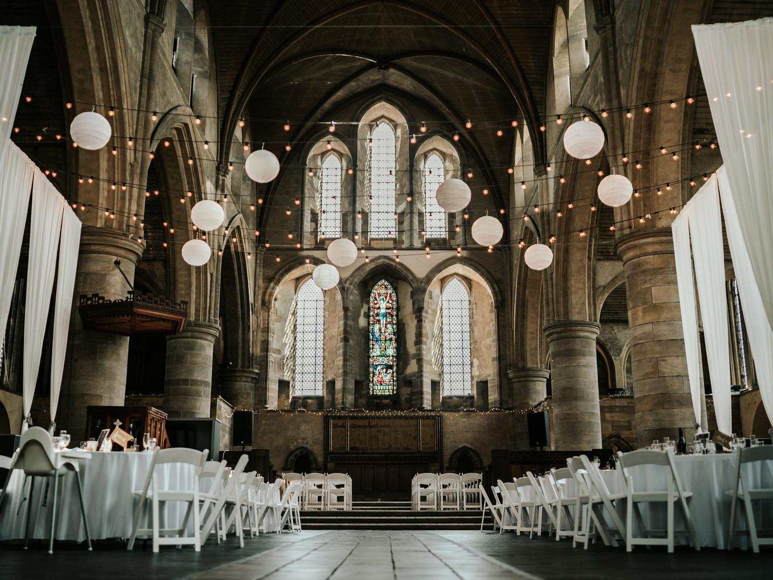 An event venue with arched stained glass windows, draped white fabric, and hanging paper lanterns at Left Bank Leeds.