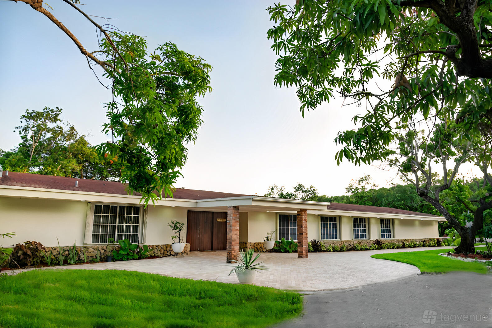 A white ranch-style barn with a paved entryway, brick pillars, and mature trees at Mon Petit