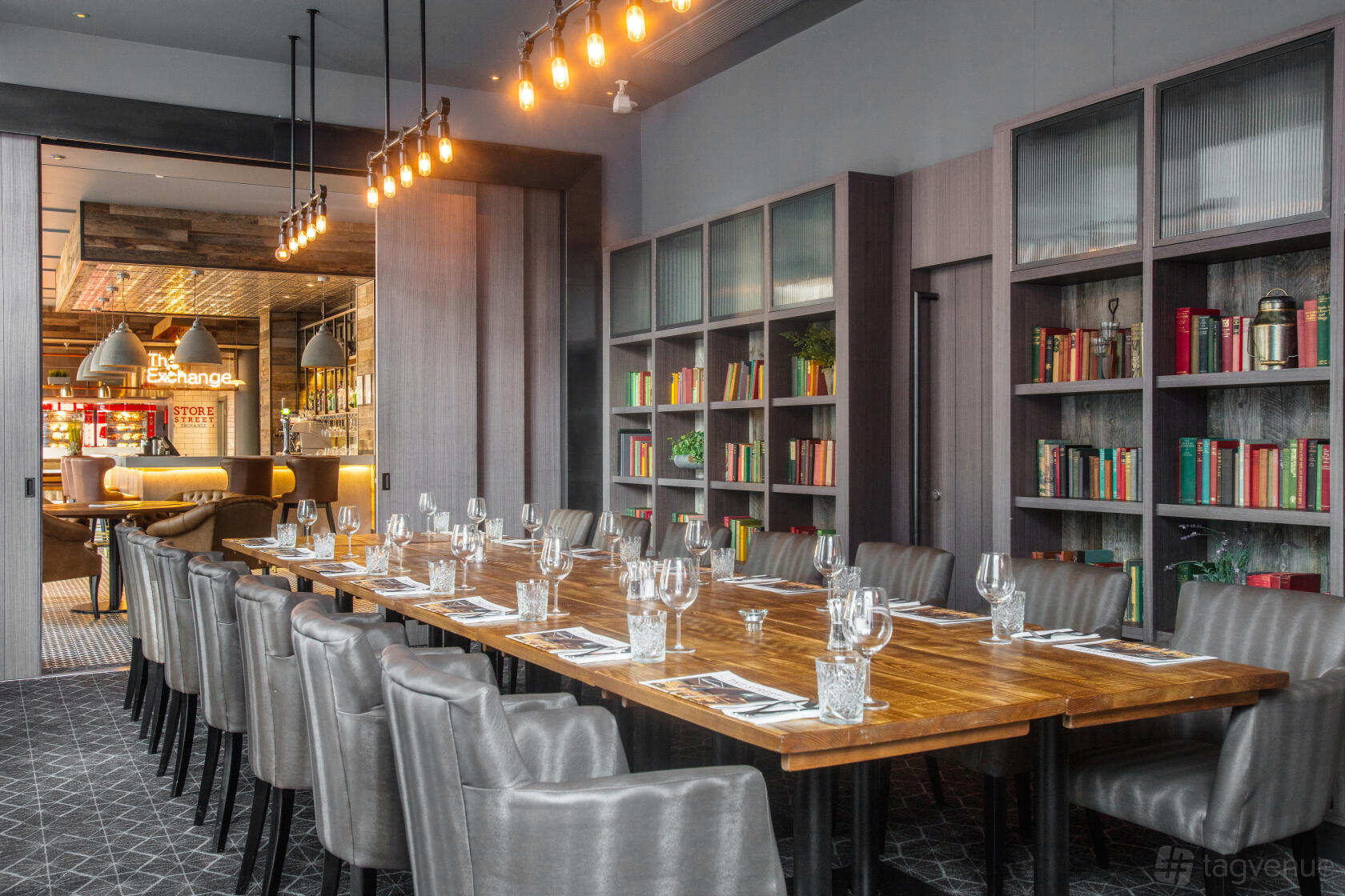 A dining room with a long wooden table, grey upholstered chairs, and bookshelves at DoubleTree by Hilton Manchester - Piccadilly.