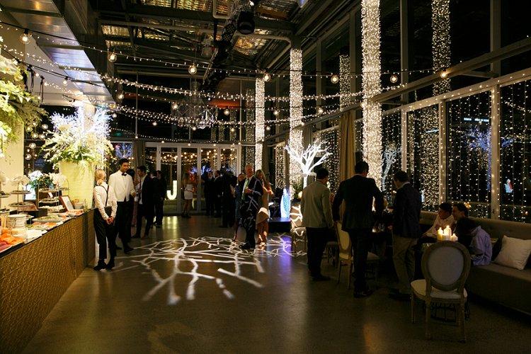 An event venue with floor-to-ceiling windows, string lights, and illuminated decorative trees at Alto Event Space.