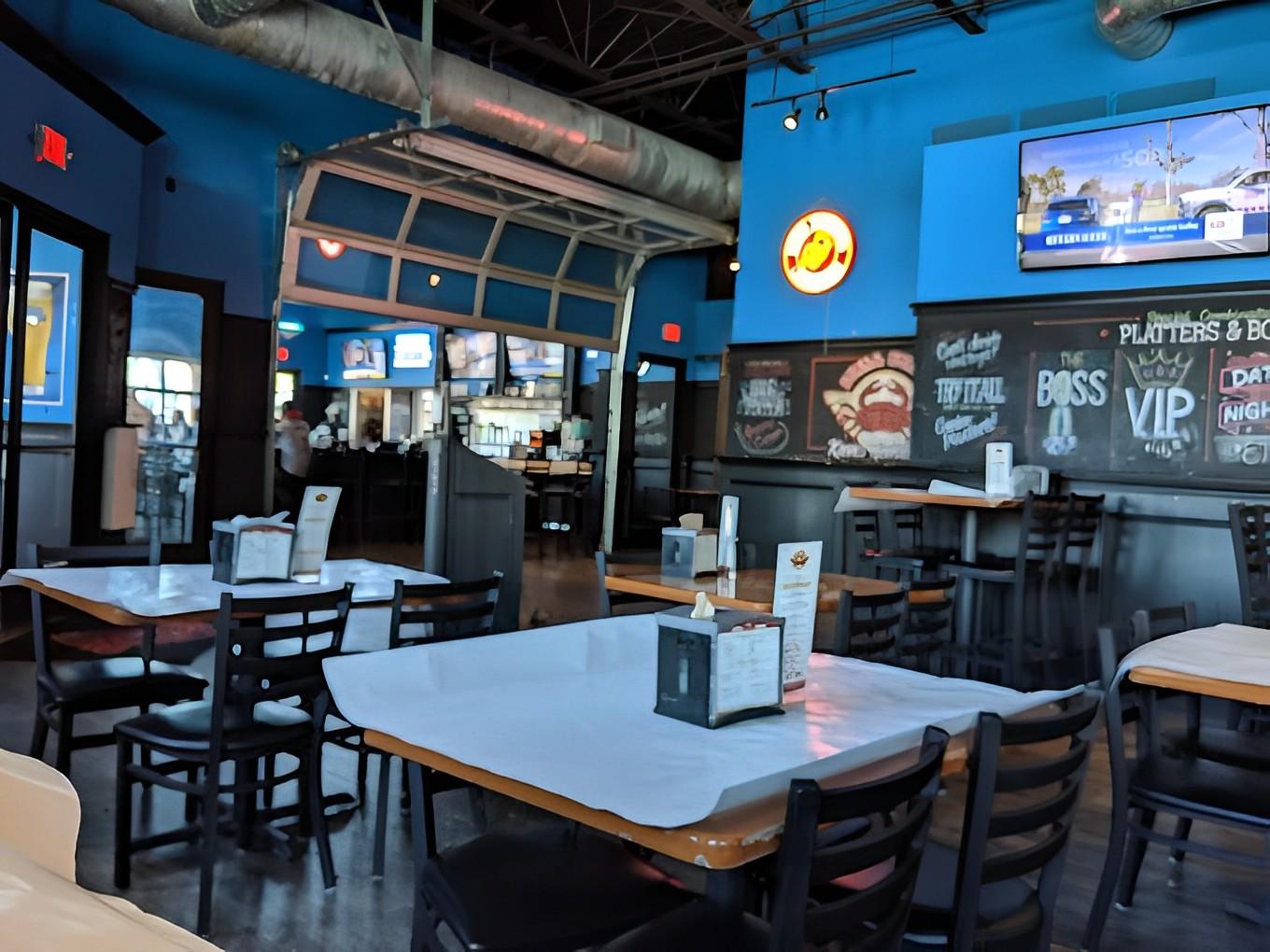 A casual restaurant with blue walls, chalkboard menus, TV screens, and paper-covered tables at Shell Shack Dallas.