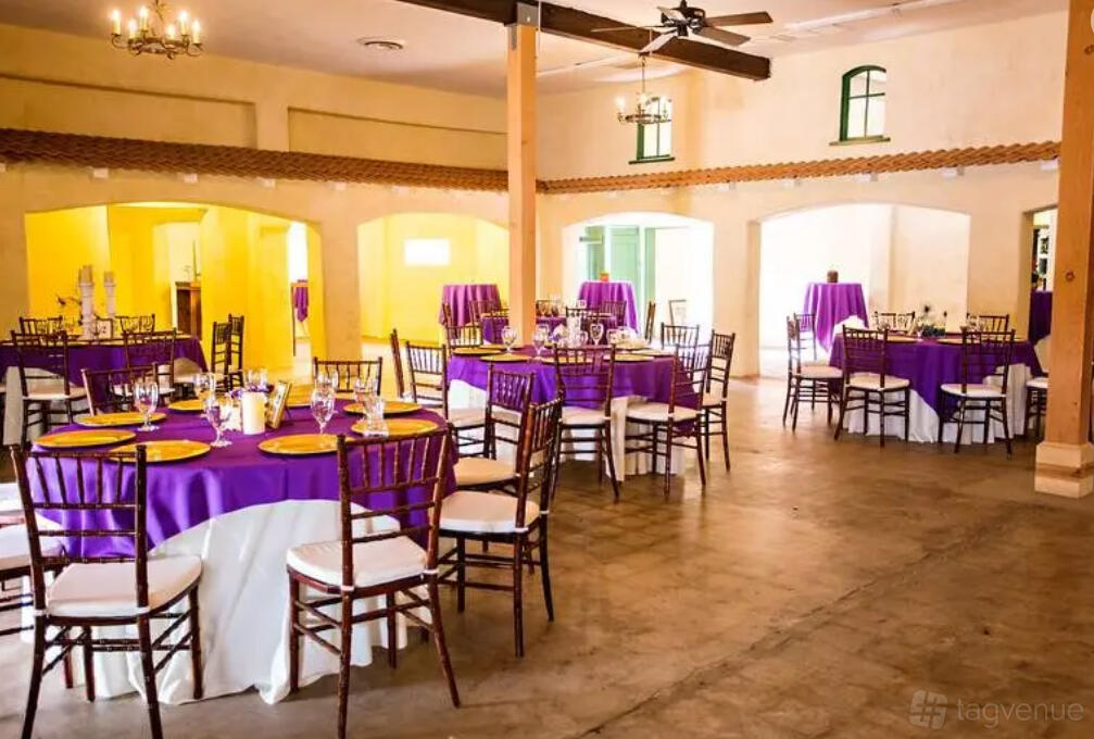A hall with round tables draped in purple linens, wooden chairs, and chandeliers at Garden Of Light.