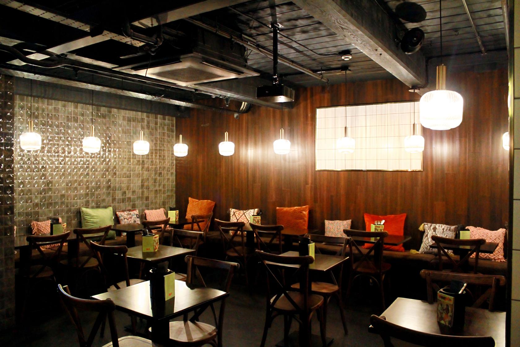 A basement lounge with wood-paneled walls, pendant lights, and cushioned bench seating at Boogalú.