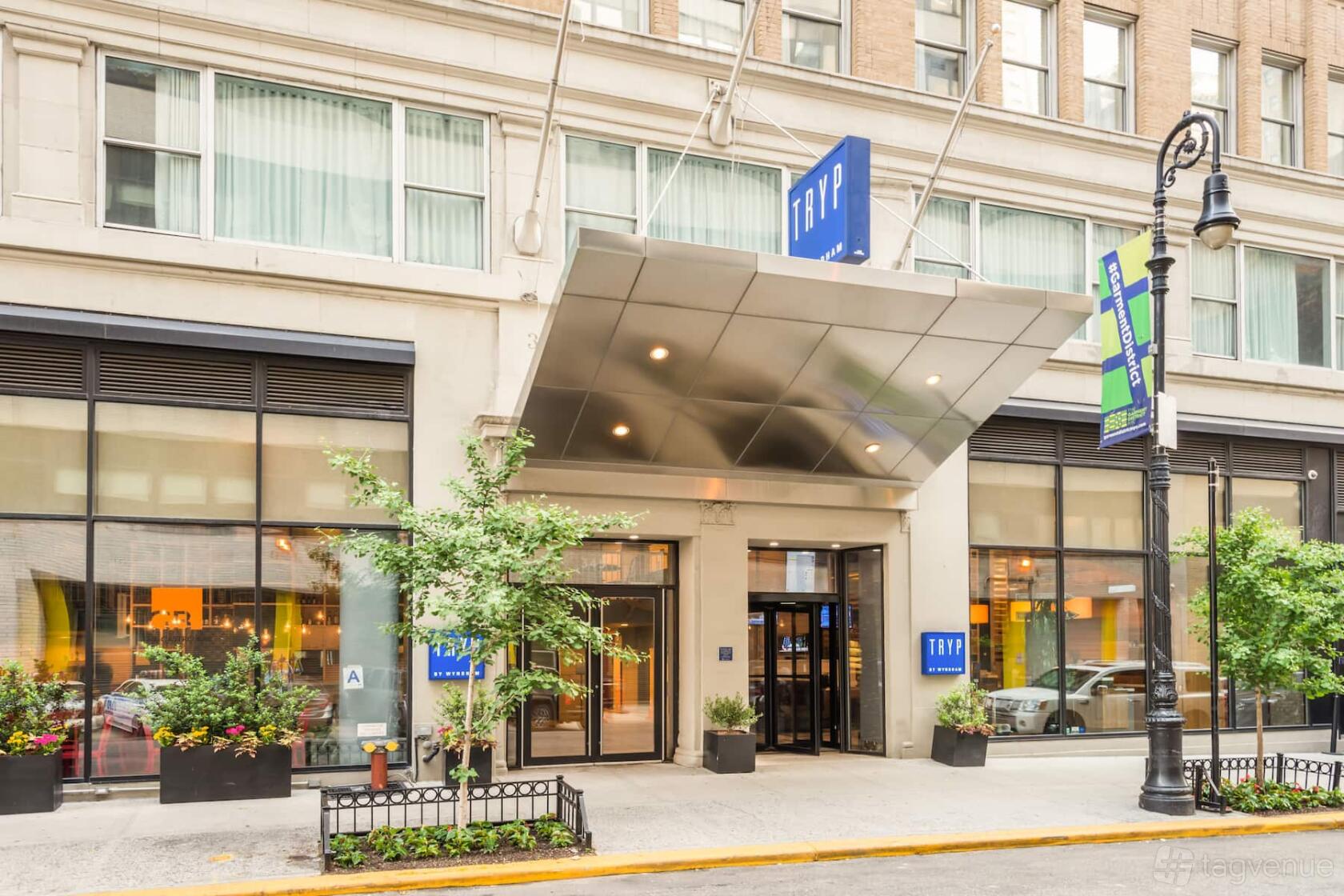 A hotel entrance with a metal canopy, glass doors, and potted plants at Tryp New York City Times Square South.