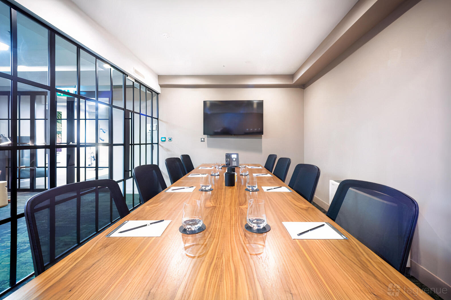 A meeting centre room with a long wooden table, black mesh chairs, glass walls, and a wall-mounted TV at Landmark: Newman Street, Fitzrovia, London.