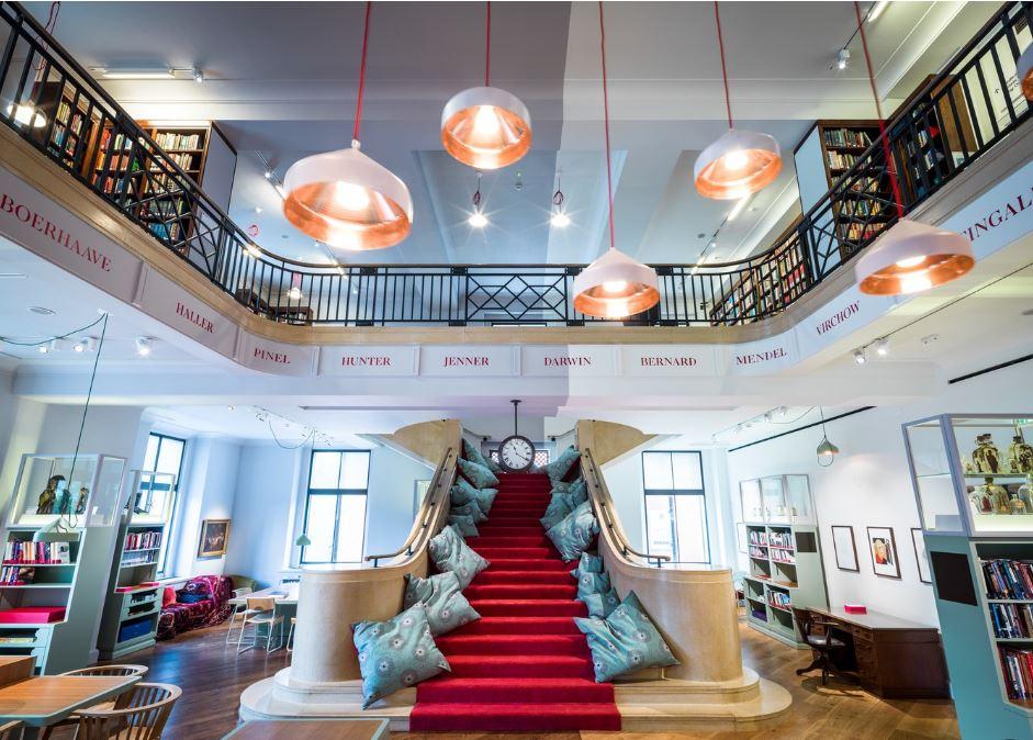 A museum library with a grand staircase, red carpet, bookshelves, and pendant lighting at Wellcome Collection.