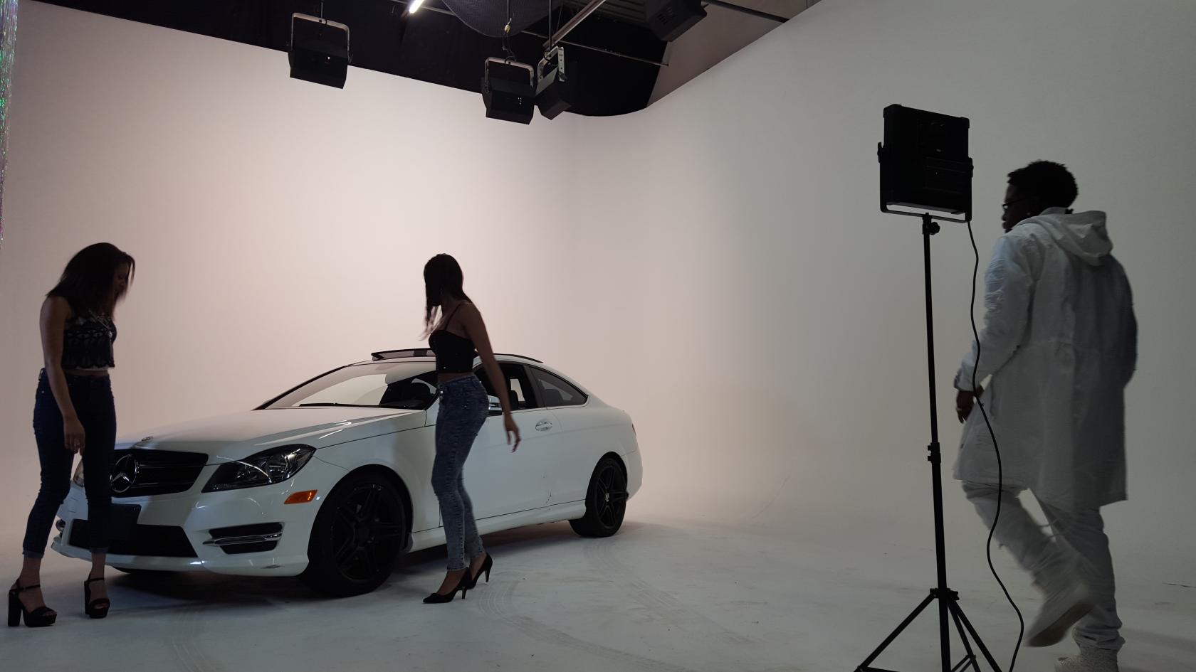 A photo and film studio with a white cyclorama wall, black ceiling rig, and a car positioned on set at Encore Film And Music Studio.