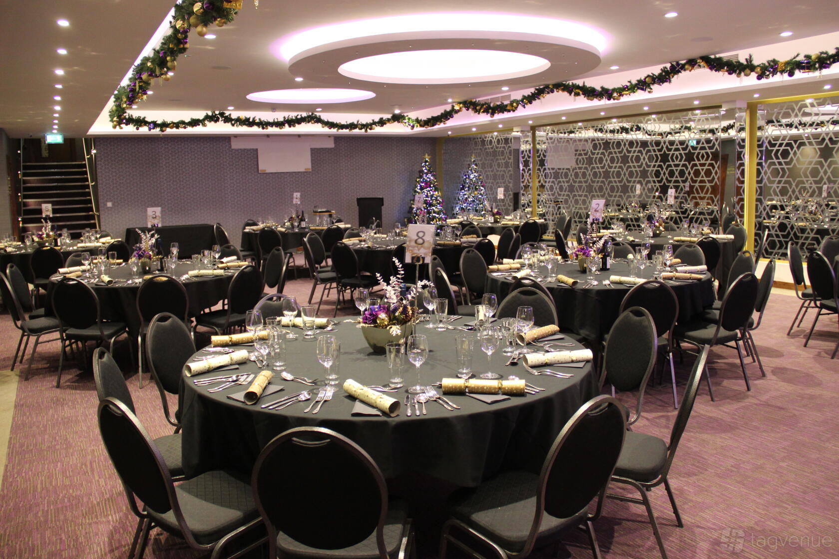 A hotel event space with round tables set for dining, festive garlands, and a decorated Christmas tree at The Place Hotel.