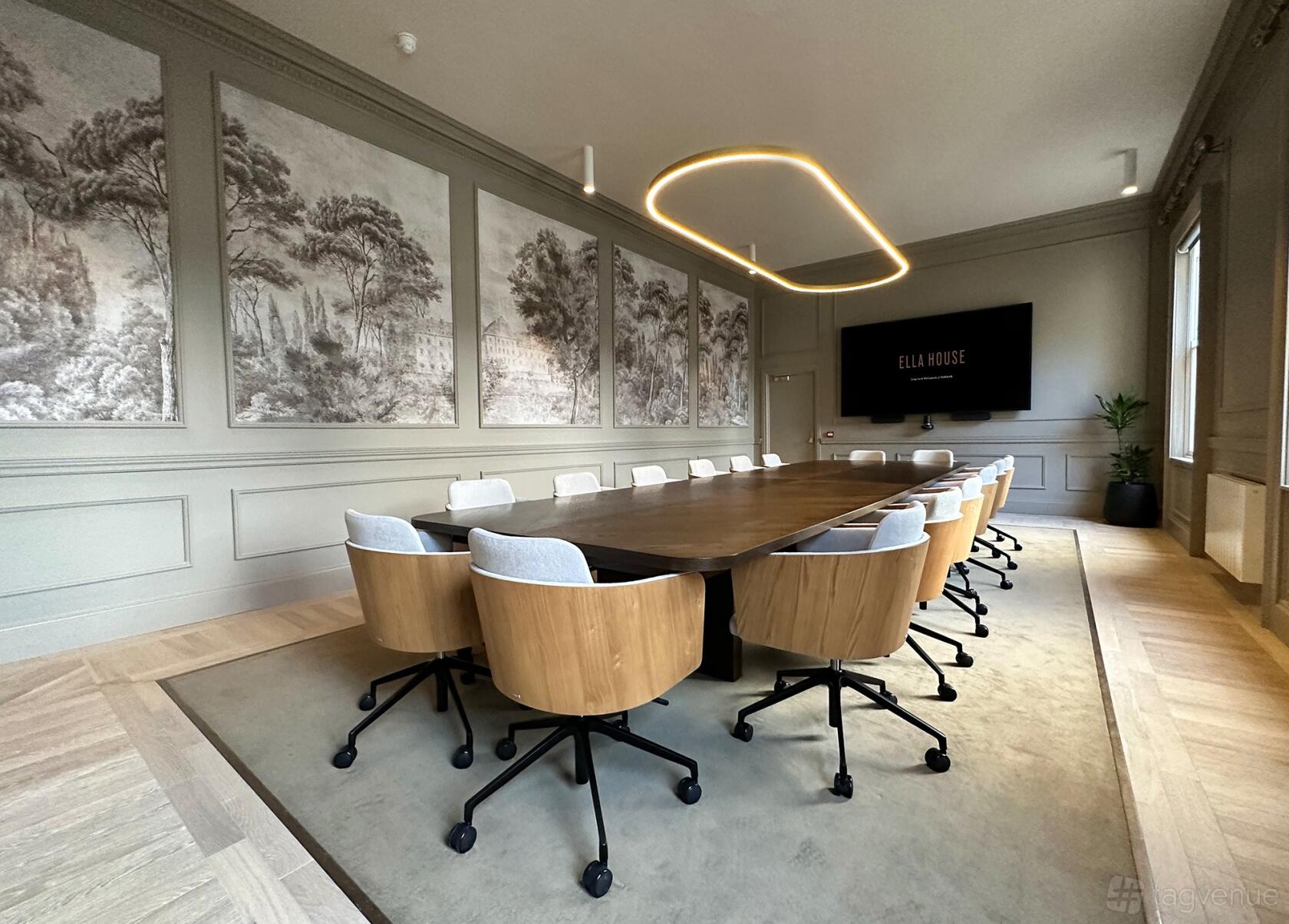 A boardroom with a long wooden table, modern chairs, wall art, and a large screen at Ella House.
