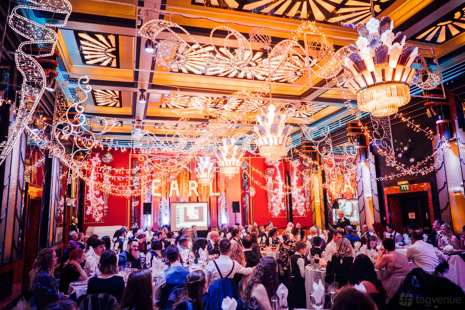 A hotel ballroom with art deco chandeliers, bold ceiling patterns, and guests seated at round tables at The Earl of Doncaster.