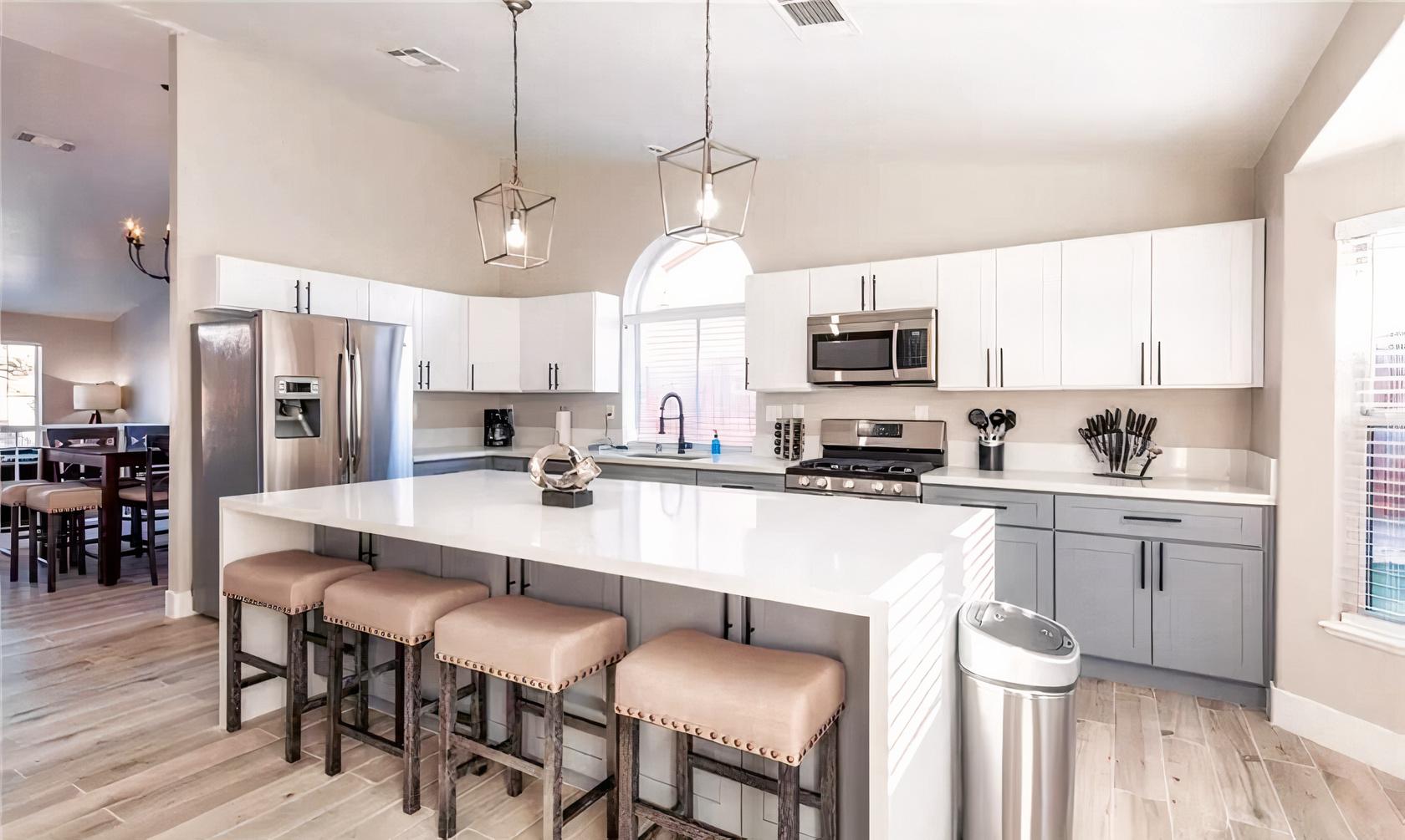 A spacious house kitchen with a large white island, stainless steel appliances, and pendant lighting at Modern Bright Resort Style Home.