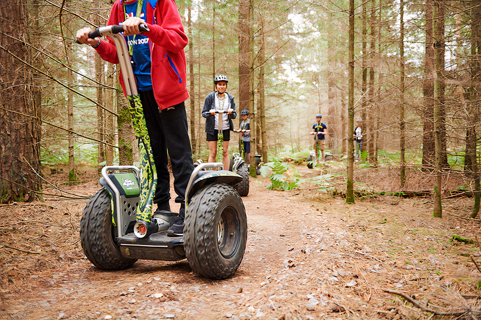 An outdoor trail with people riding Segways among tall pine trees at Go Ape Bracknell.