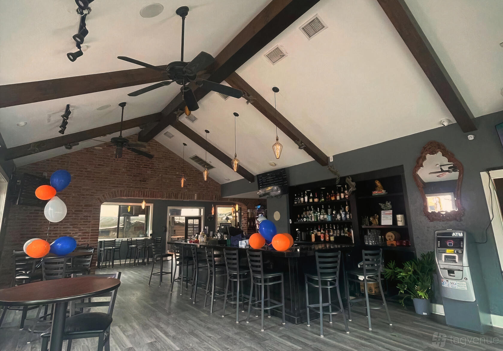 An event space in a restaurant with exposed brick walls, vaulted ceiling with wooden beams, bar seating, and decorative lighting at Velvet Oak Tavern.