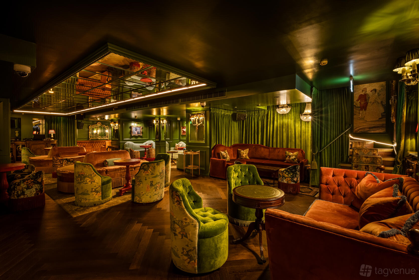 A bar in a nightclub with velvet armchairs, mirrored ceiling, and green draped walls at Dear Darling Mayfair.