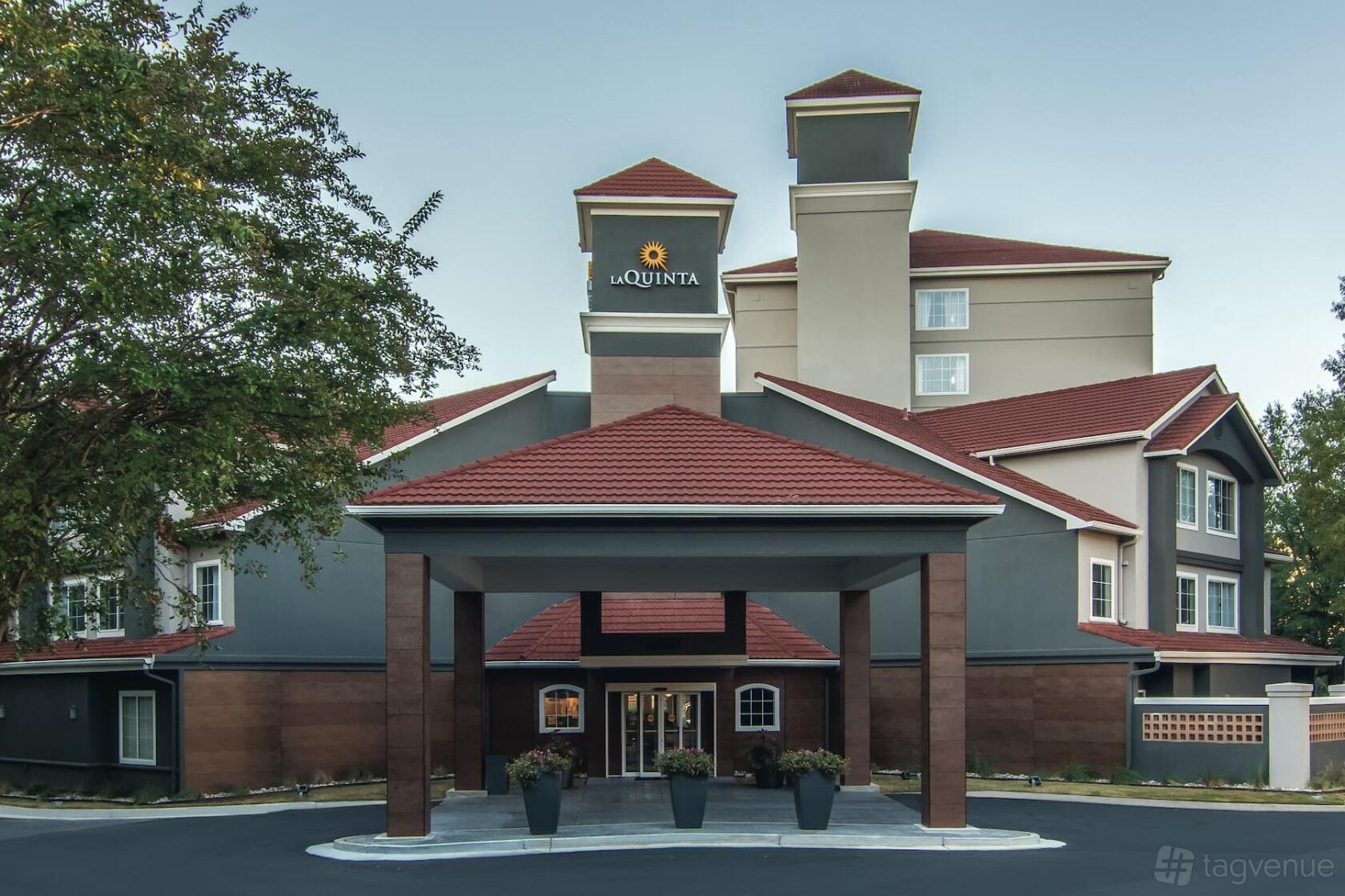 A hotel entrance with a covered driveway, red tile roof, and potted plants at La Quinta Inn & Suites by Atlanta Perimeter.