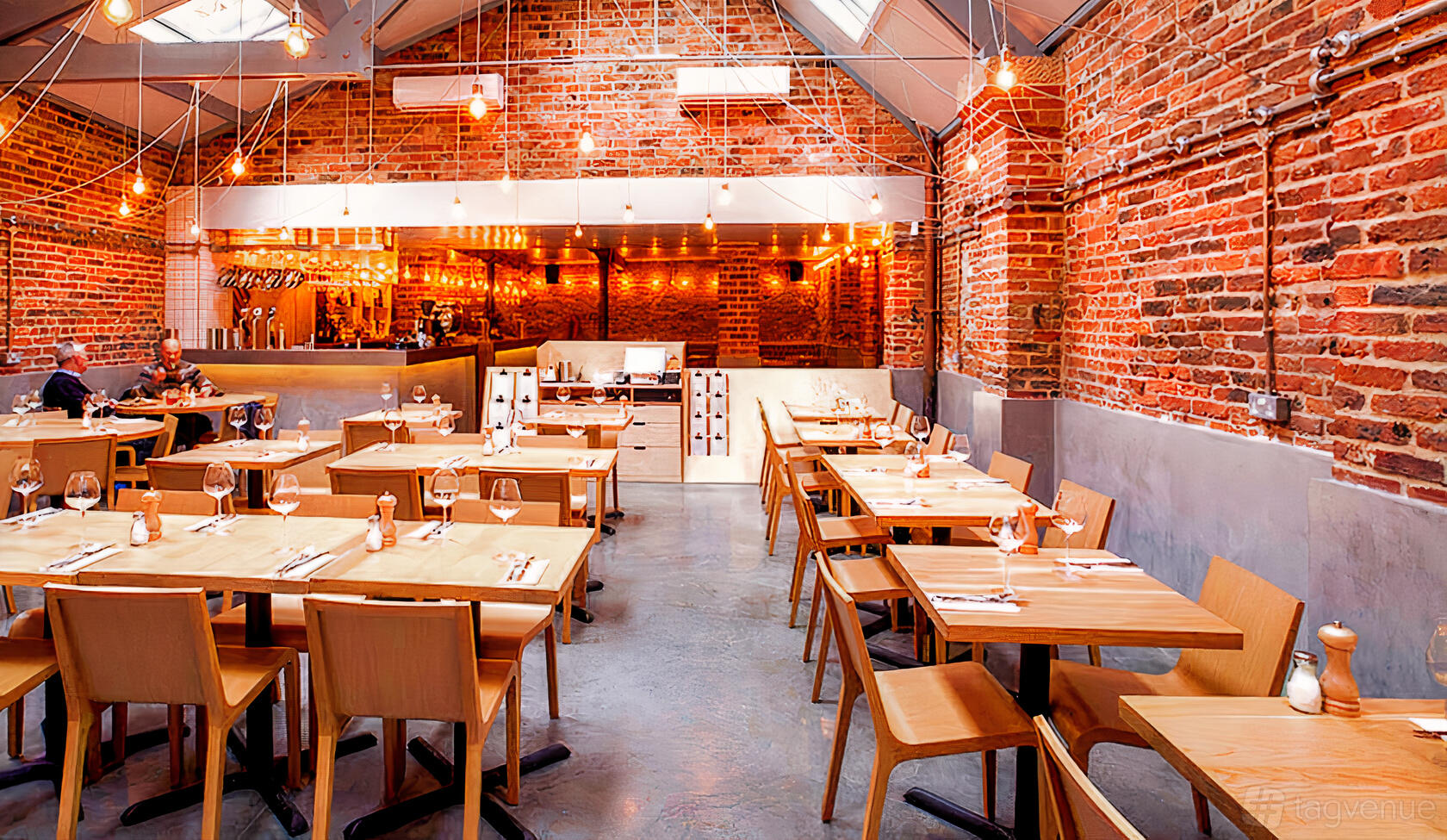 A restaurant with exposed brick walls, wooden tables, pendant lighting, and an open ceiling at Shears Yard.