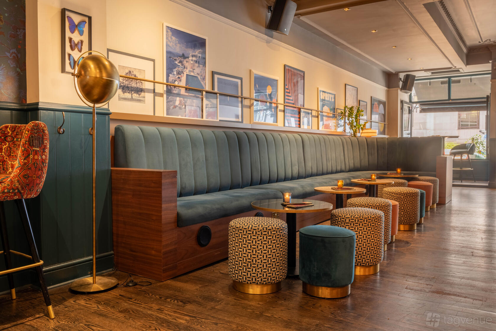 An event space in a cocktail bar with a long green velvet banquette, patterned stools, and framed wall art at LOCKES Bar Covent Garden.