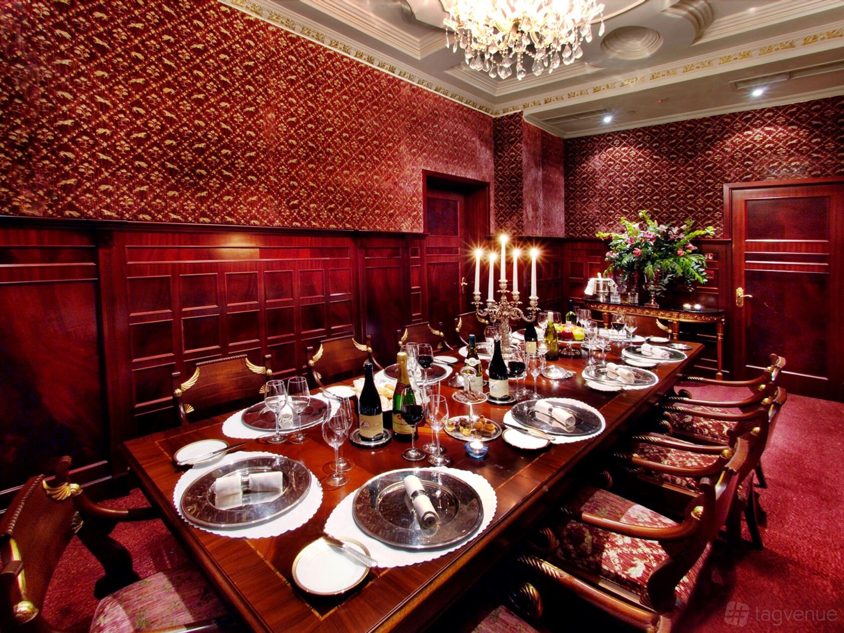 A hotel dining room with wood-paneled walls, a chandelier, and a long table set with silverware and candles at The Bentley London.