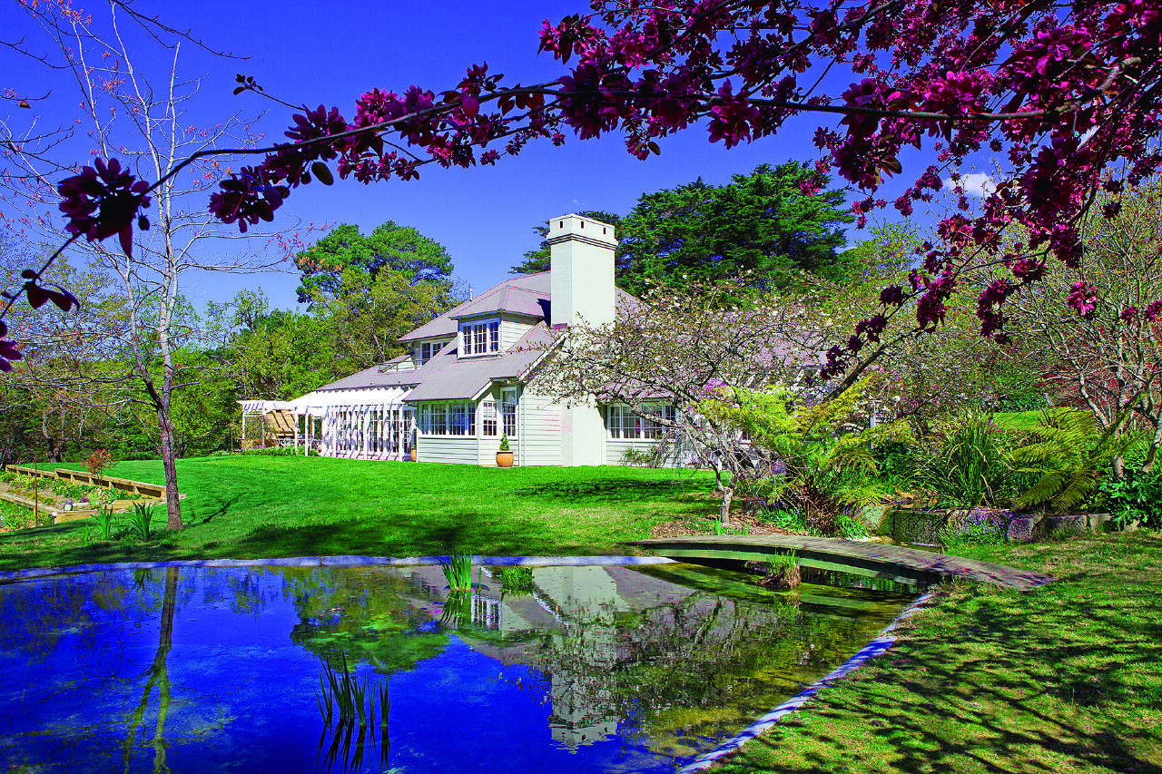 An outdoor space with a reflective lake, manicured lawn, and blooming trees at Parklands Country Garden & Lodges.