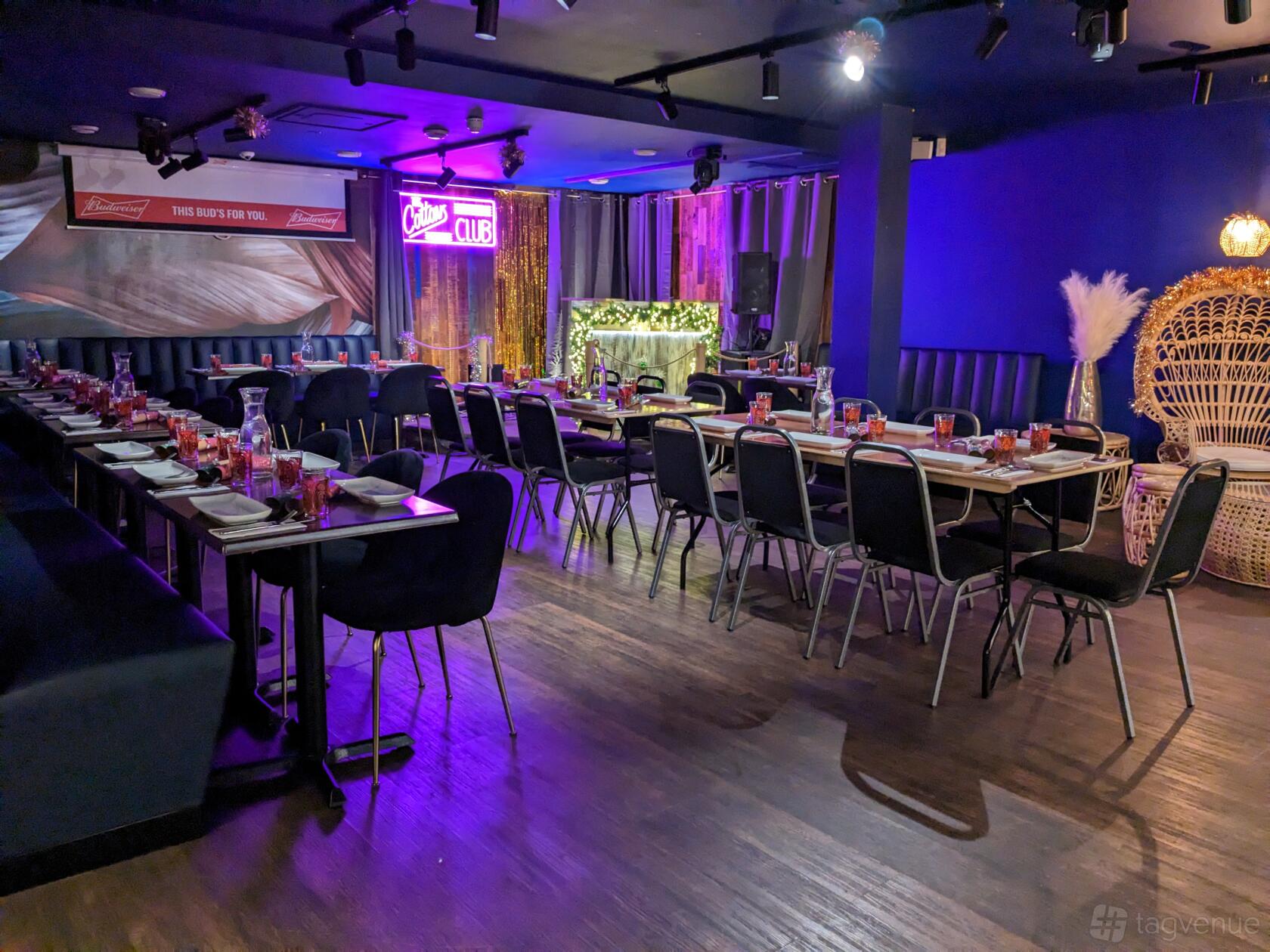 A function room with banquet tables, dark wood floors, and a neon sign at Cottons Shoreditch.