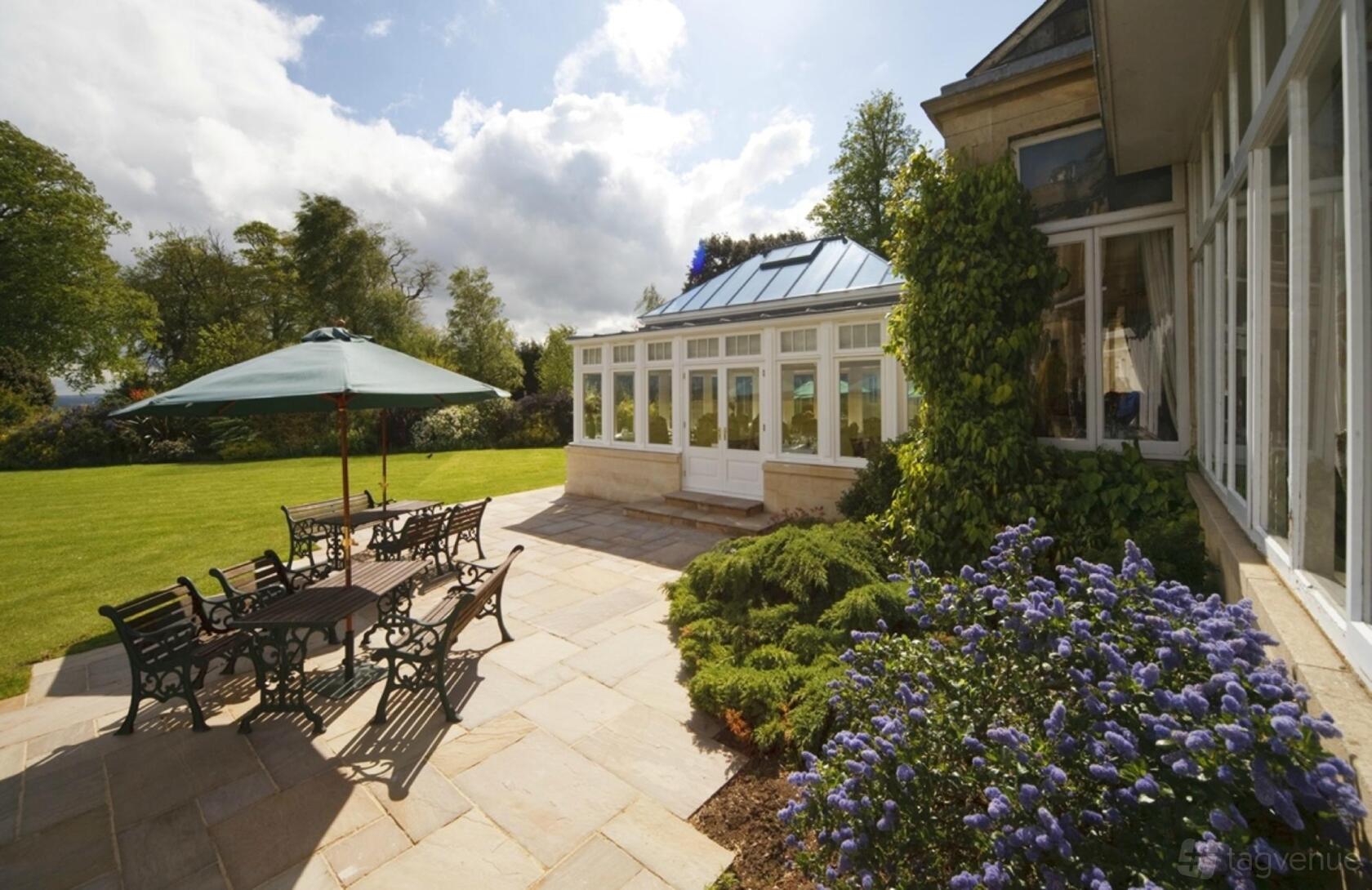 A hotel event space with a stone patio, outdoor seating, sun umbrella, and glass conservatory at Leigh Park Hotel.