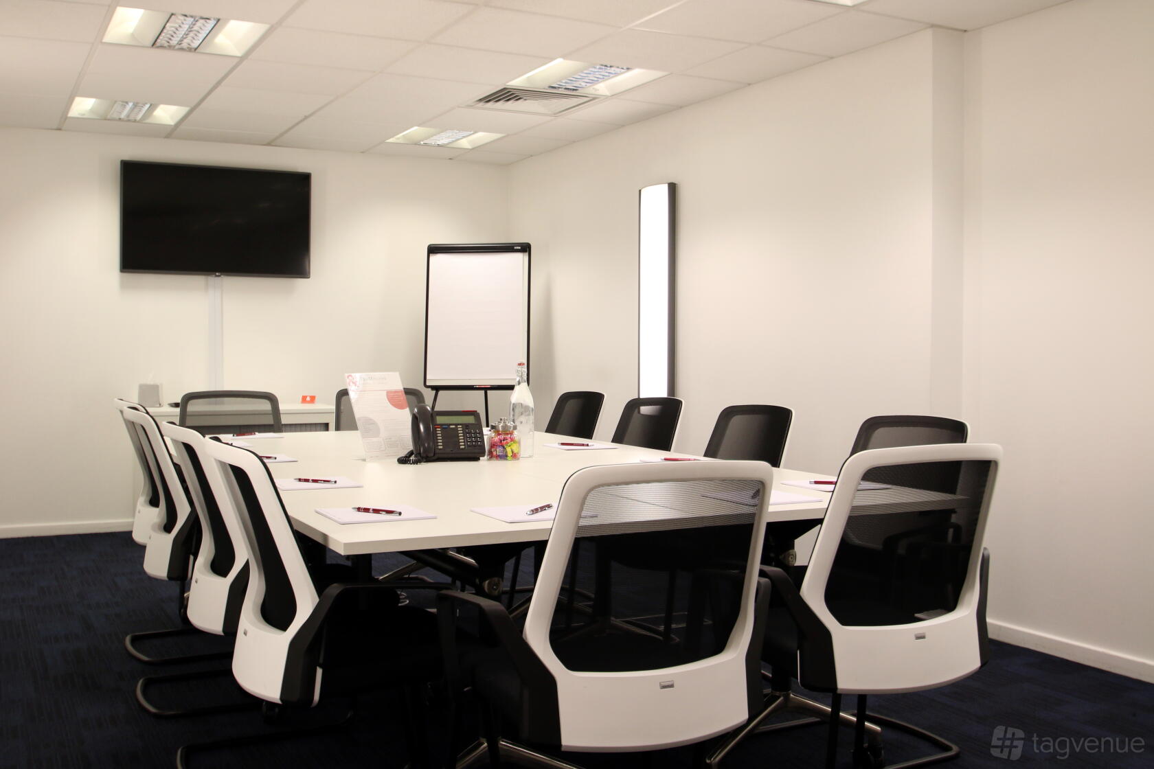 A meeting room with a large rectangular table, ergonomic chairs, wall-mounted TV, and flipchart at 150 Minories.
