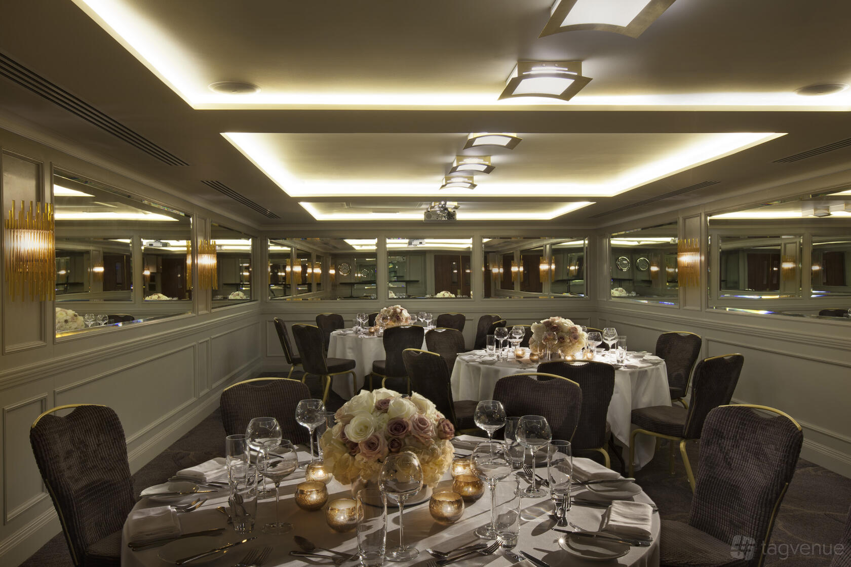 An event space with round tables dressed in white linens, floral centerpieces, and wall mirrors at Radisson Blu Hotel, London Euston Square.