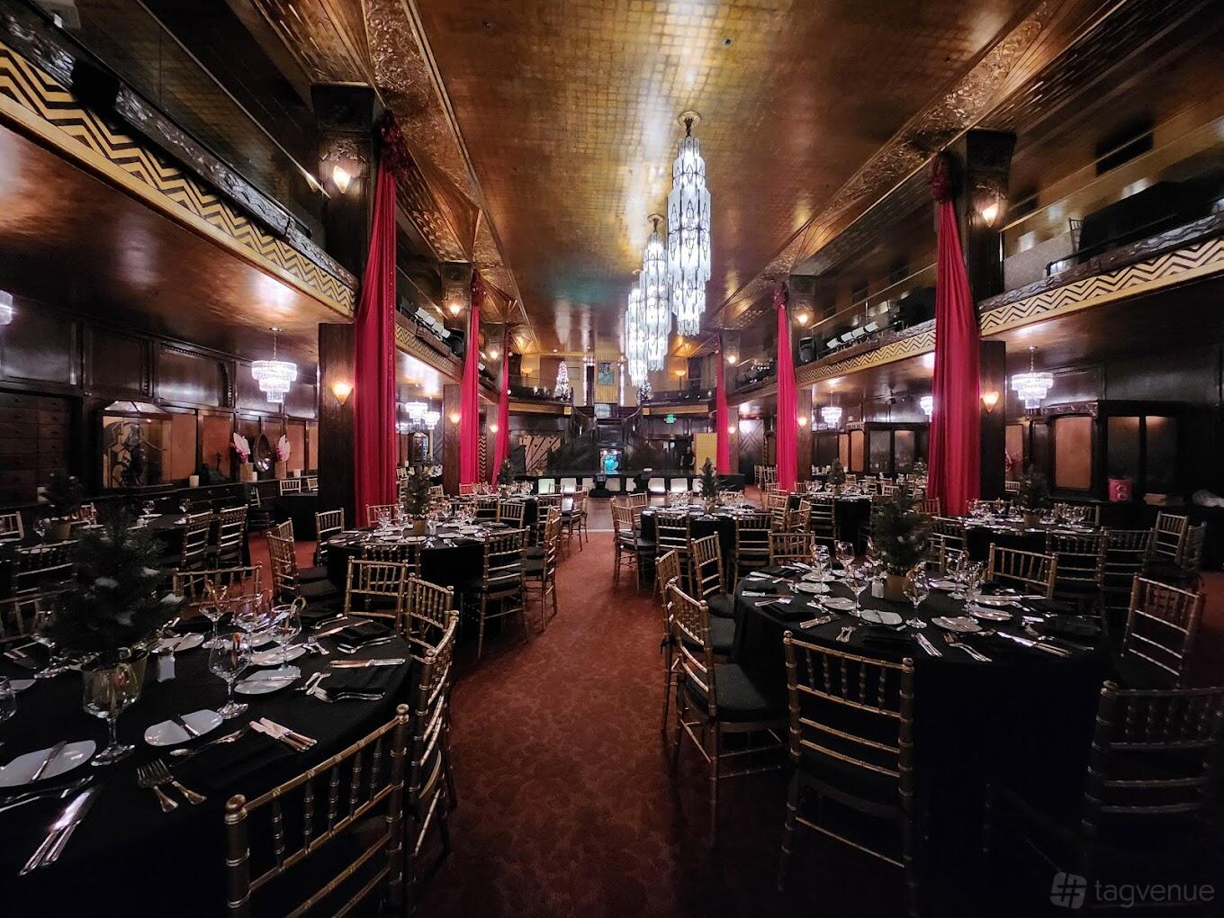 A restaurant with gold ceilings, art deco chandeliers, round tables with black linens, and red drapes at Cicada Restaurant and Lounge.