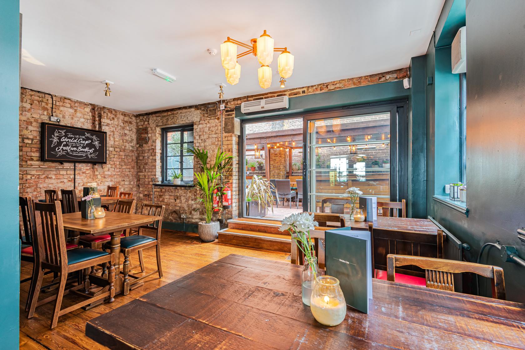 A pub terrace with exposed brick walls, wooden tables, and a glass door opening to an outdoor deck at Carpenters Arms.